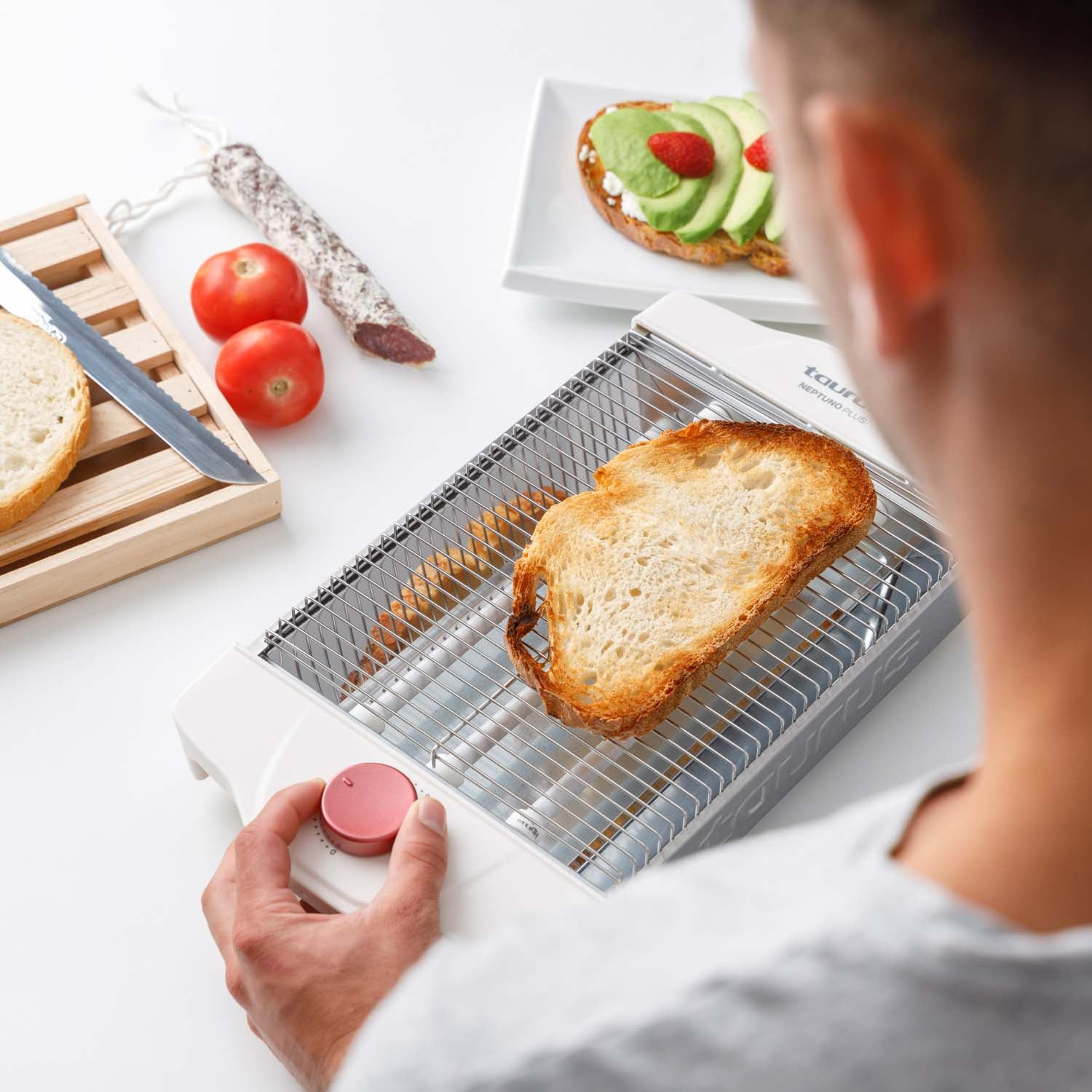 Toster z kromką tostów i osobą regulującą ustawienia, z produktami spożywczymi.