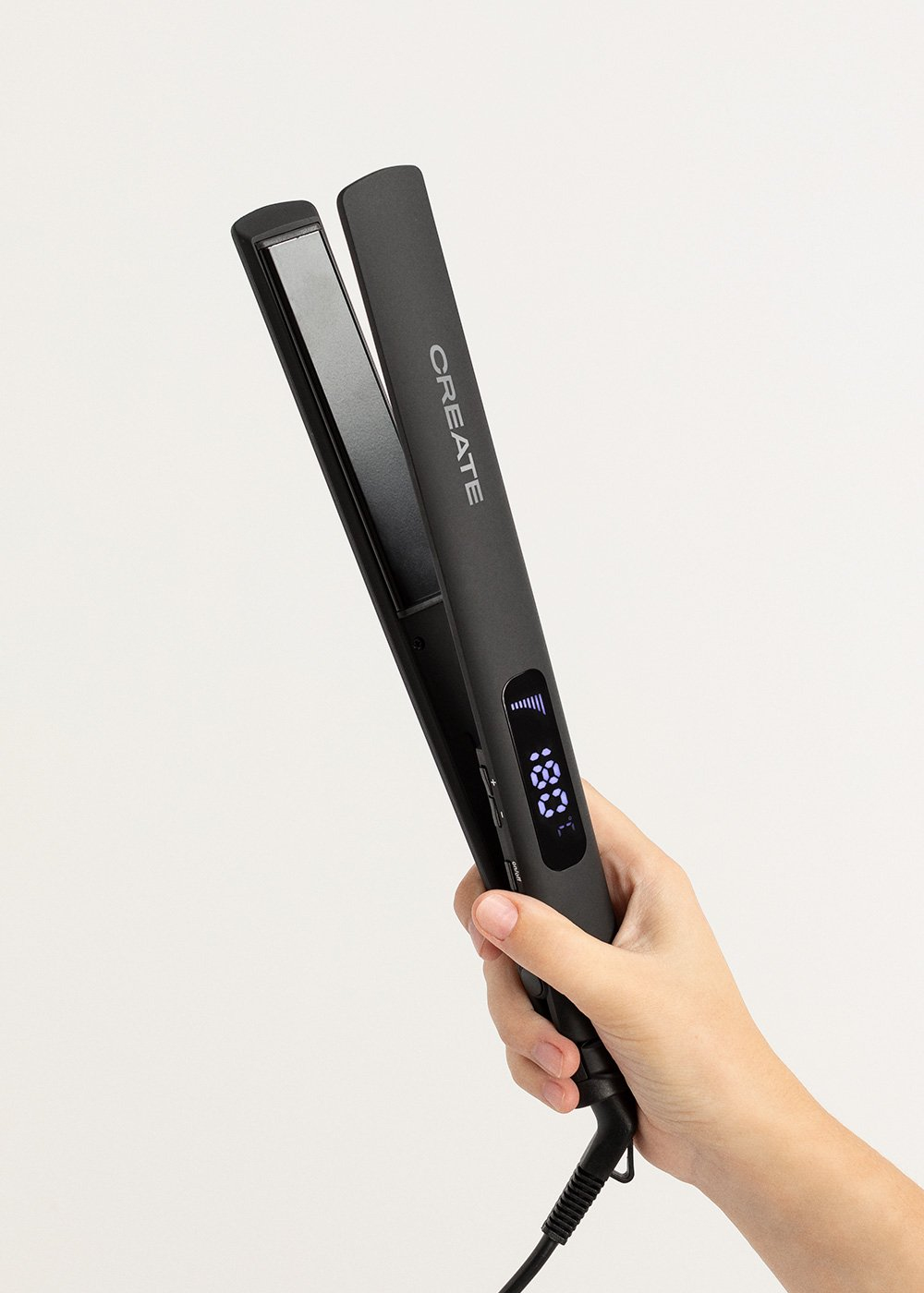 Una persona sosteniendo una plancha de pelo negra con una pantalla digital, sobre un fondo blanco.