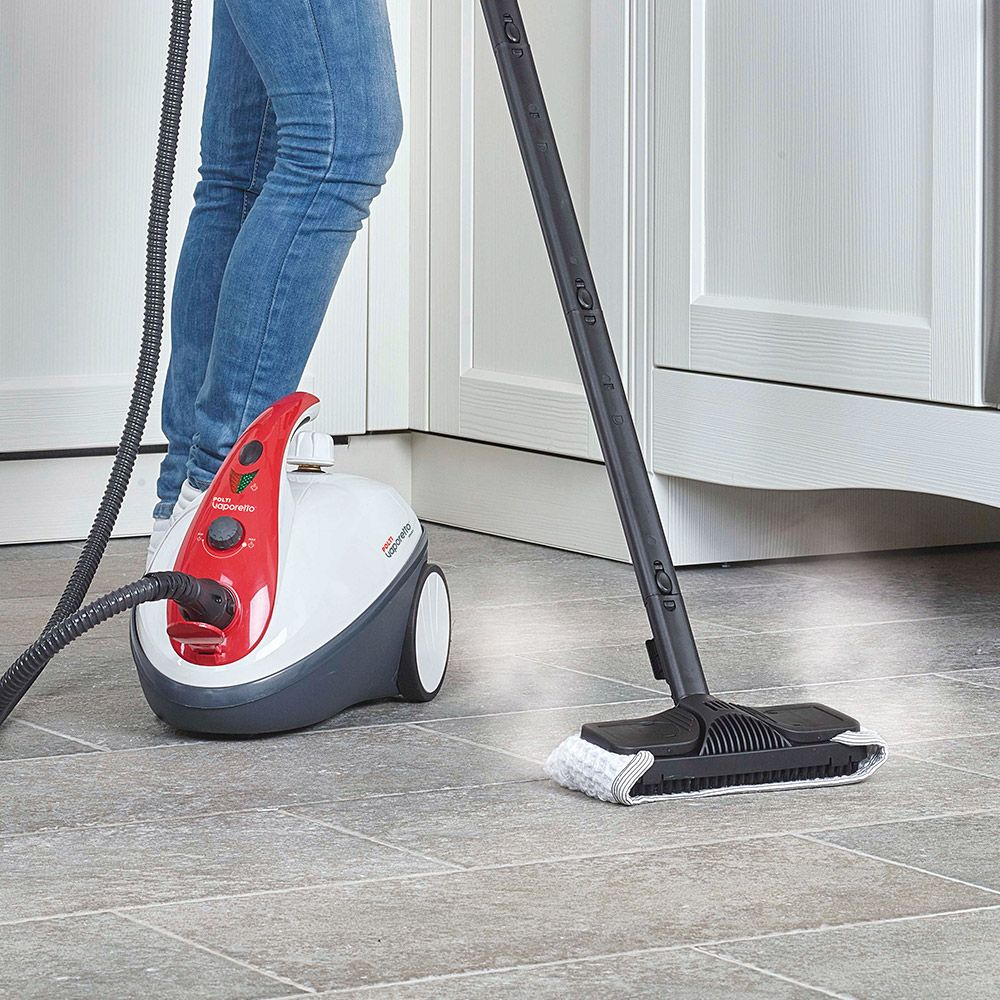 Osoba czyści podłogę za pomocą parownicy. Biało-czerwona parownica z czarnym wężem i dyszą.