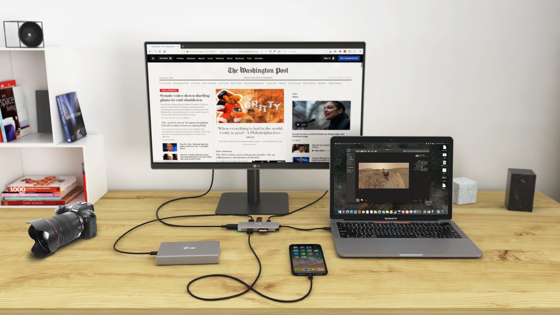 Scrivania con un monitor che mostra un sito web, un laptop, una fotocamera e un telefono collegati a un hub.