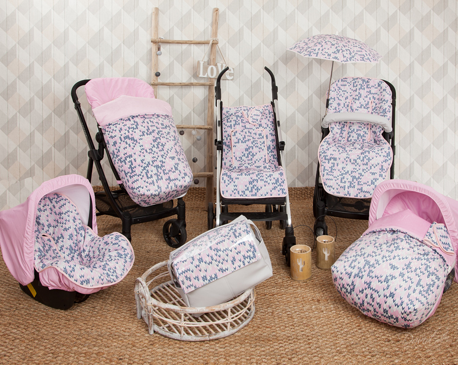 Un conjunto de accesorios para cochecito de bebé en rosa y azul, incluyendo un asiento de coche y una bolsa, sobre una alfombra.