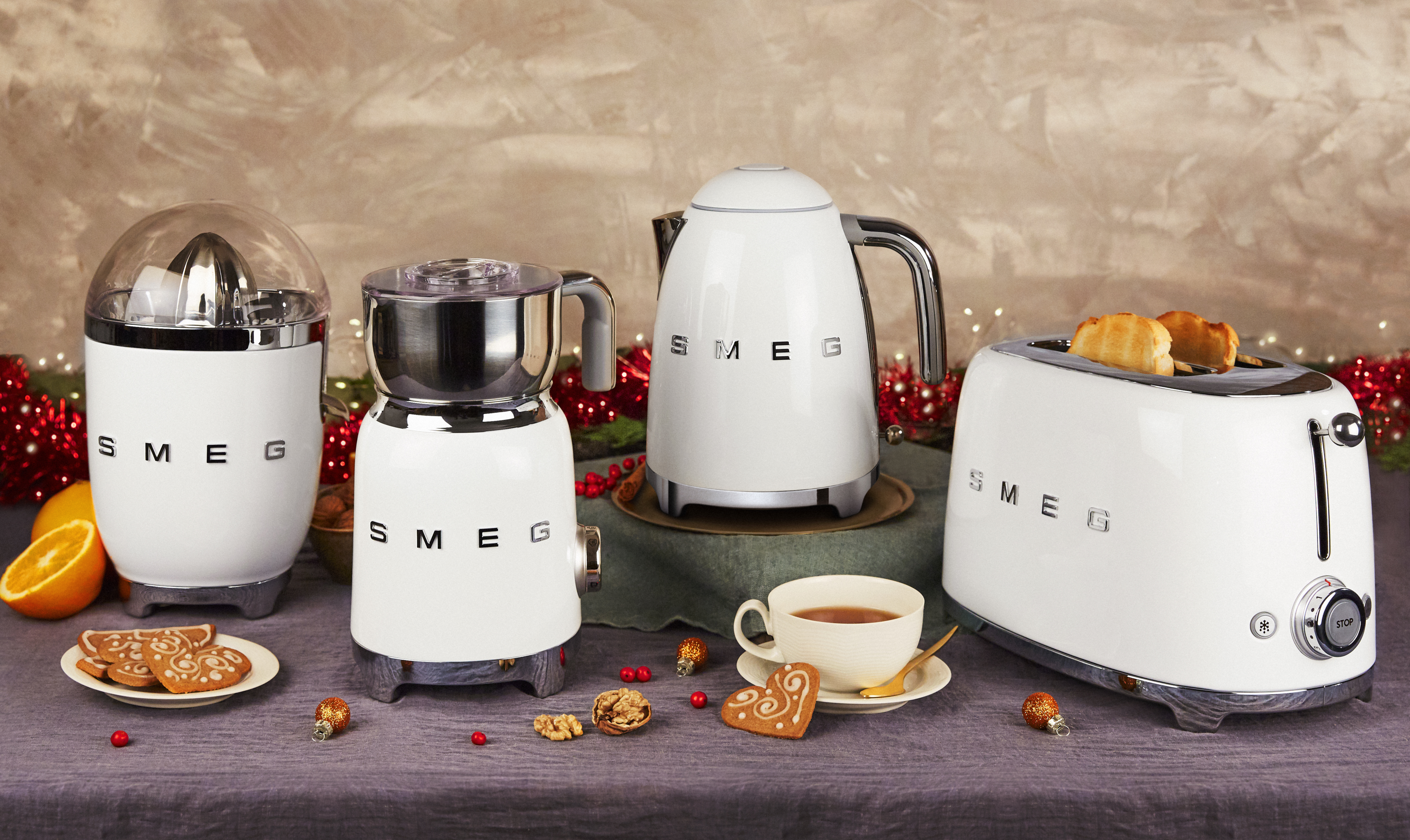 Un set di elettrodomestici da cucina SMEG bianchi, tra cui uno spremiagrumi, un macinacaffè, un bollitore e un tostapane, su un tavolo.