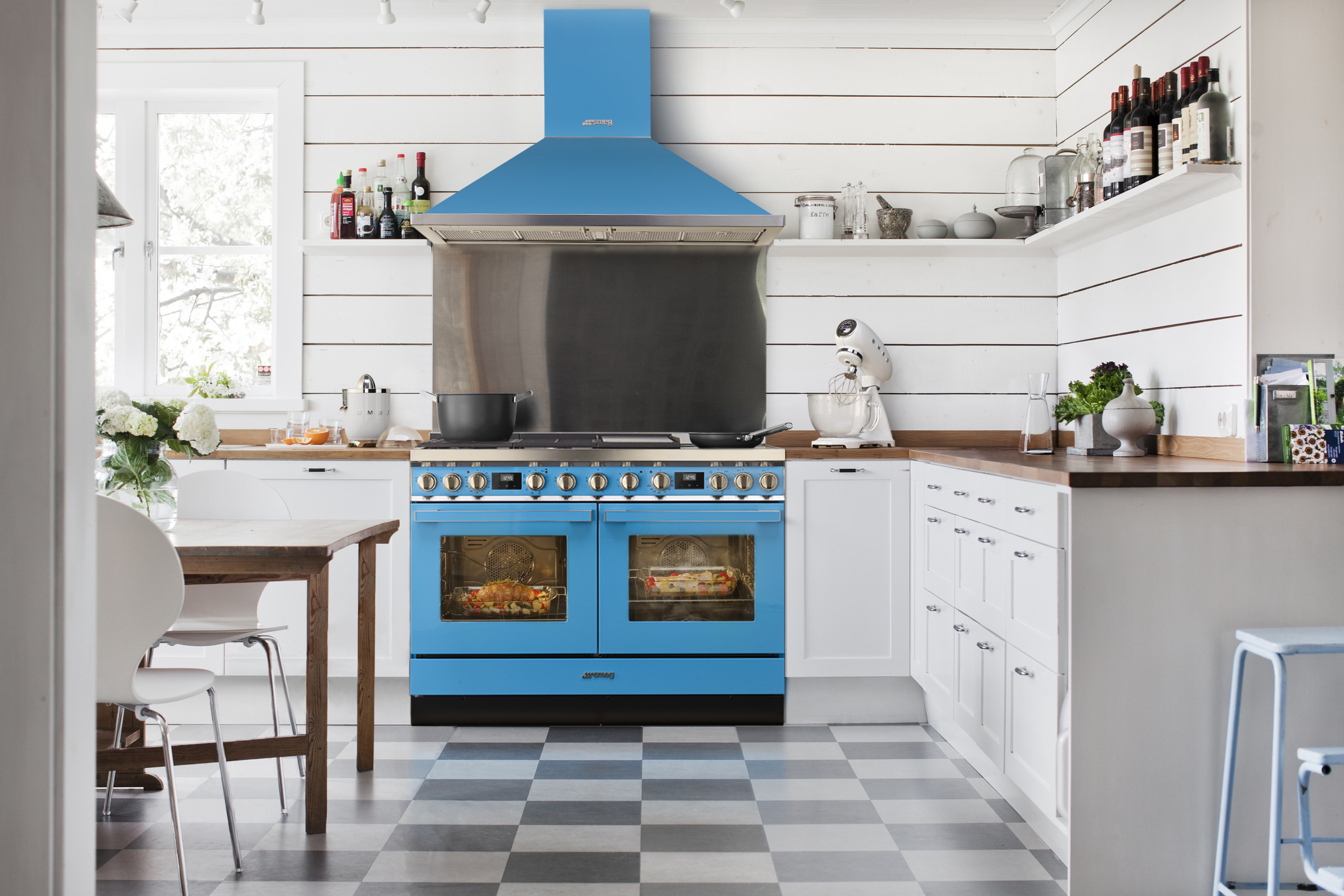 Una cucina blu con una stufa, armadi e un pavimento a scacchi. Anche una cappa aspirante è visibile.