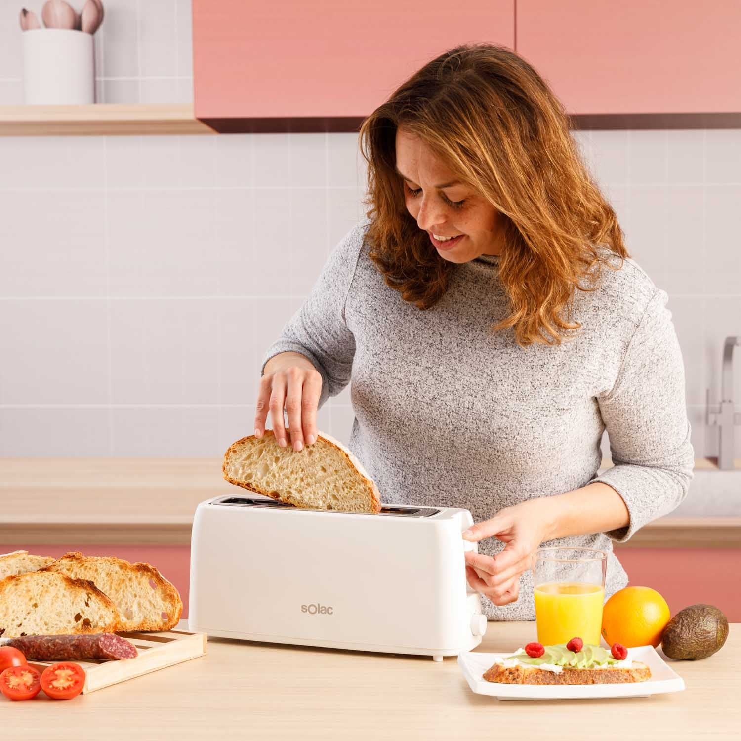 Kobieta opieka chleb w białym tosterze, z jedzeniem na stole, drewnianym tle.