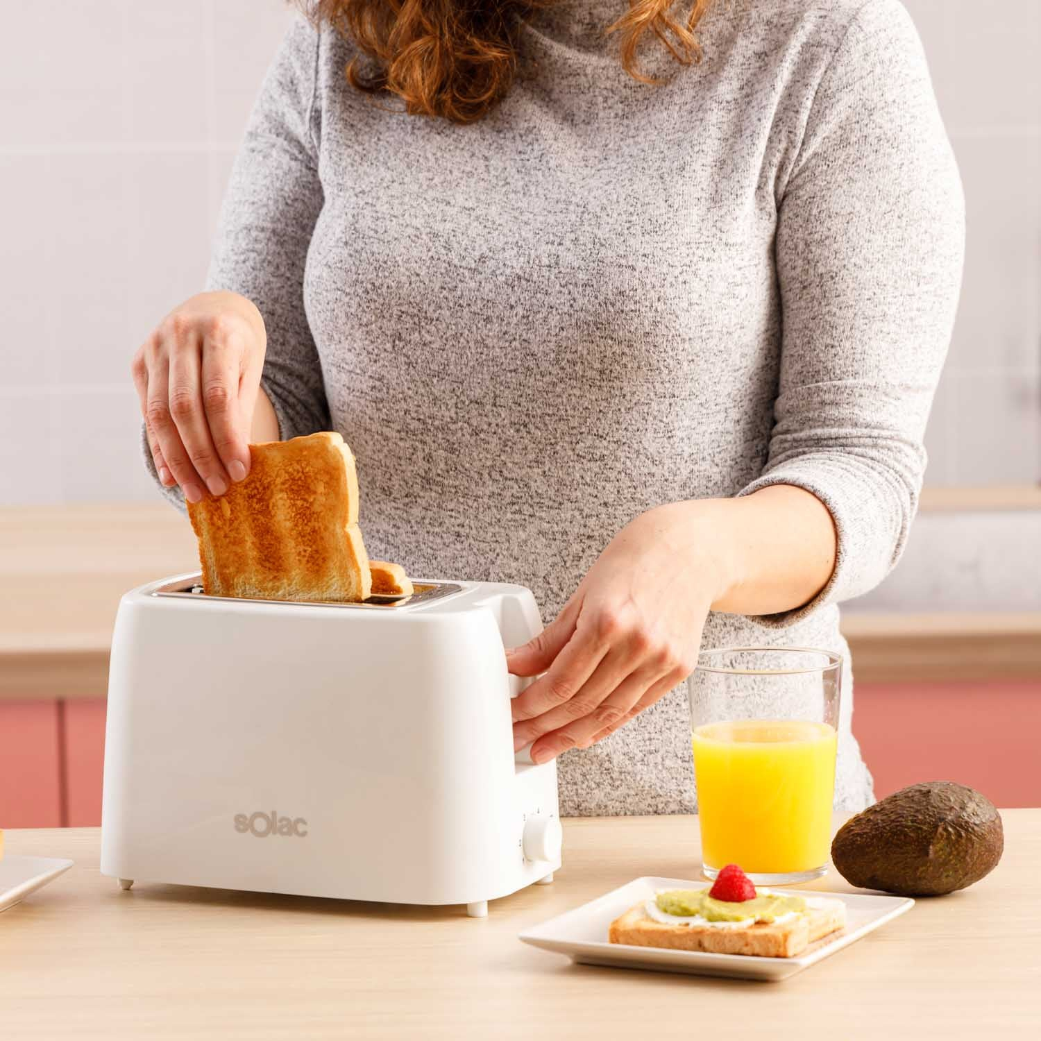 Osoba opieka chleb w białym tosterze Solac, z sokiem i awokado.