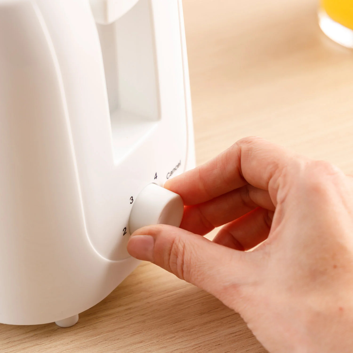 Ręka obracająca pokrętło białego tostera. Pokrętło ma liczby od 2 do 4 i anuluj.