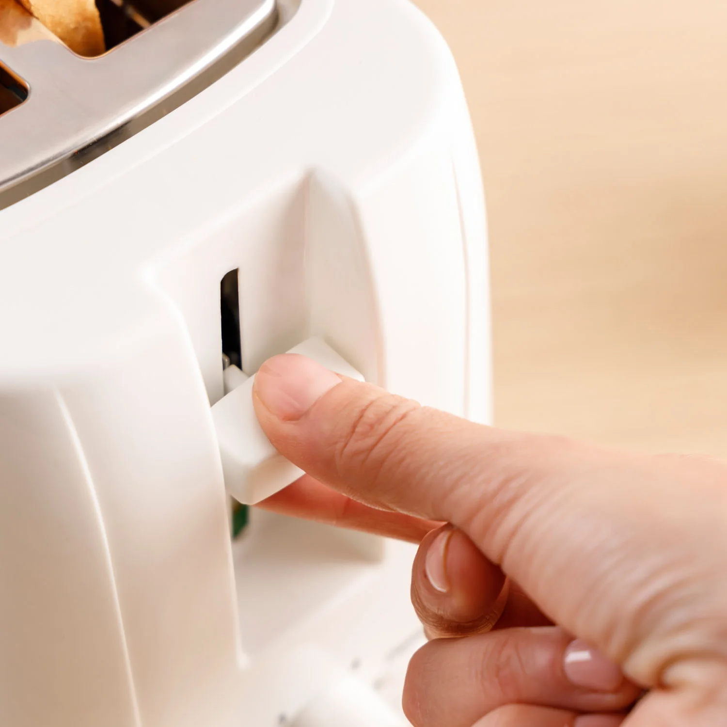 Ręka naciska dźwignię w białym tosterze.