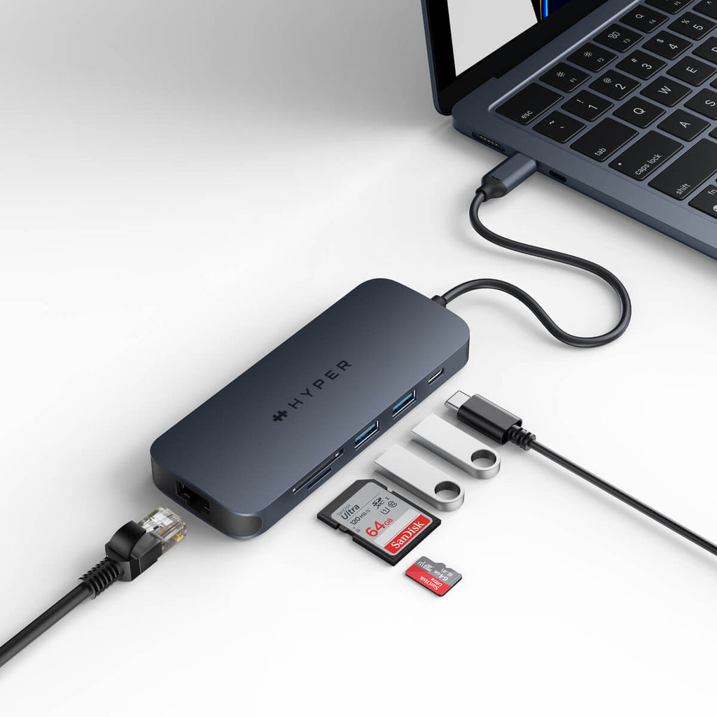 Un concentrador gris oscuro con múltiples puertos conectado a una laptop con dispositivos USB y un cable Ethernet.