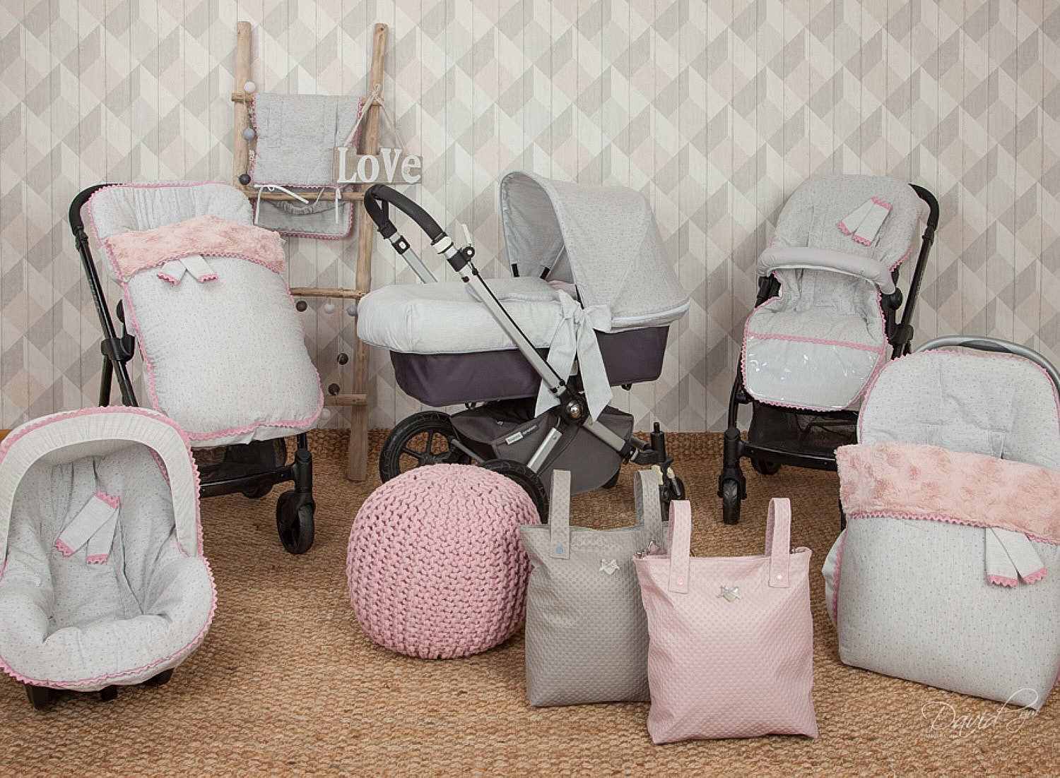 Artículos para bebés: un cochecito, un asiento para el automóvil y accesorios en un cuarto de niños con un tema rosa claro.