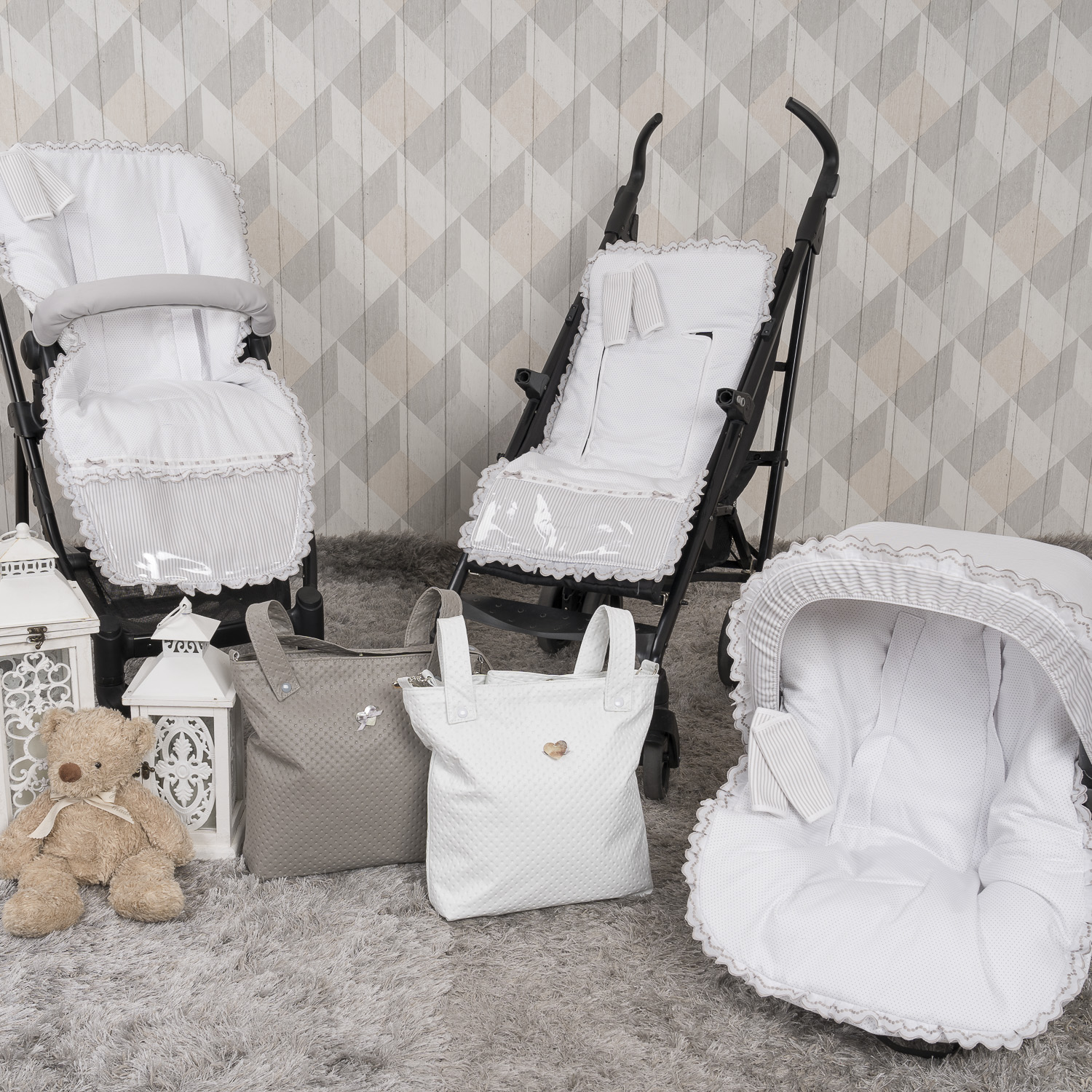 Juego de bebé con cochecito, silla de coche y bolsos. Combinación de colores gris y blanco. Oso de peluche en el suelo.