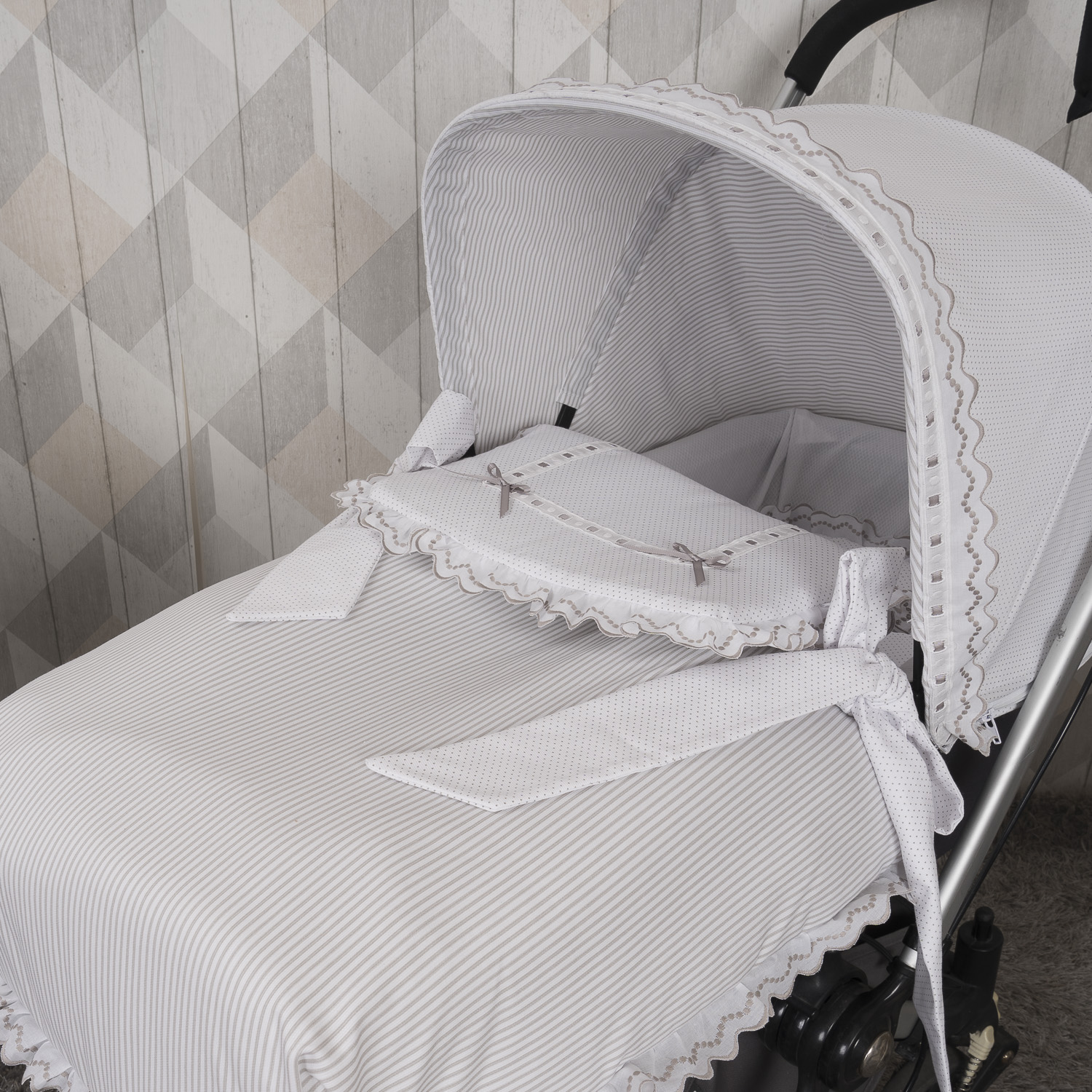 Un cochecito a rayas blancas y grises con un interior blanco y gris con cintas.