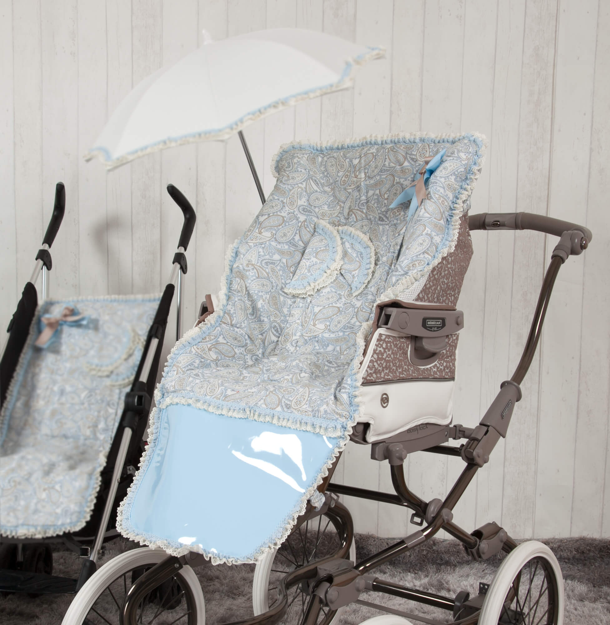 Un cochecito de bebé con diseño de paisley azul y blanco, sombrilla a juego. Otro cochecito en el fondo.