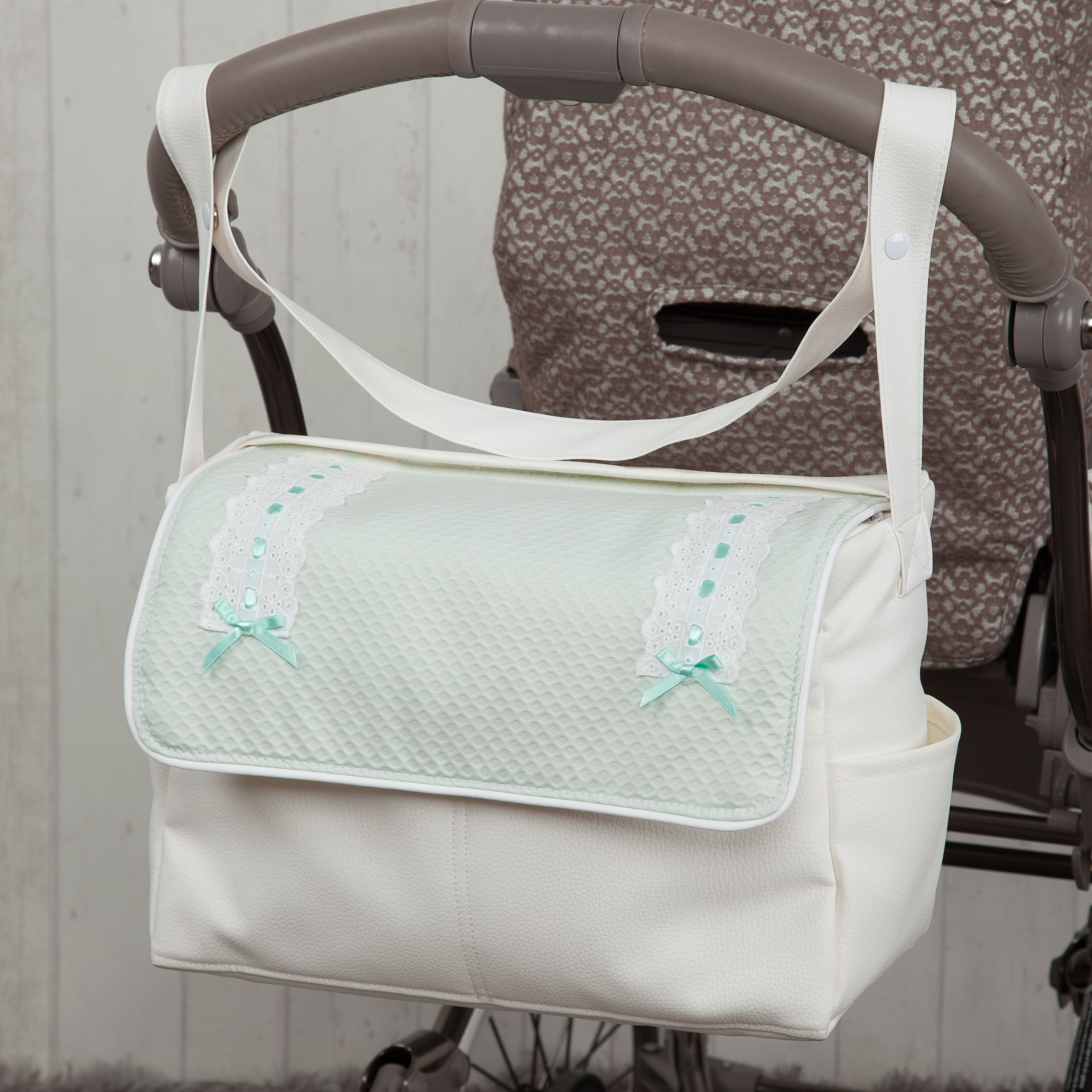 Bolso de bebé blanco y verde menta en un cochecito frente a una pared de madera.