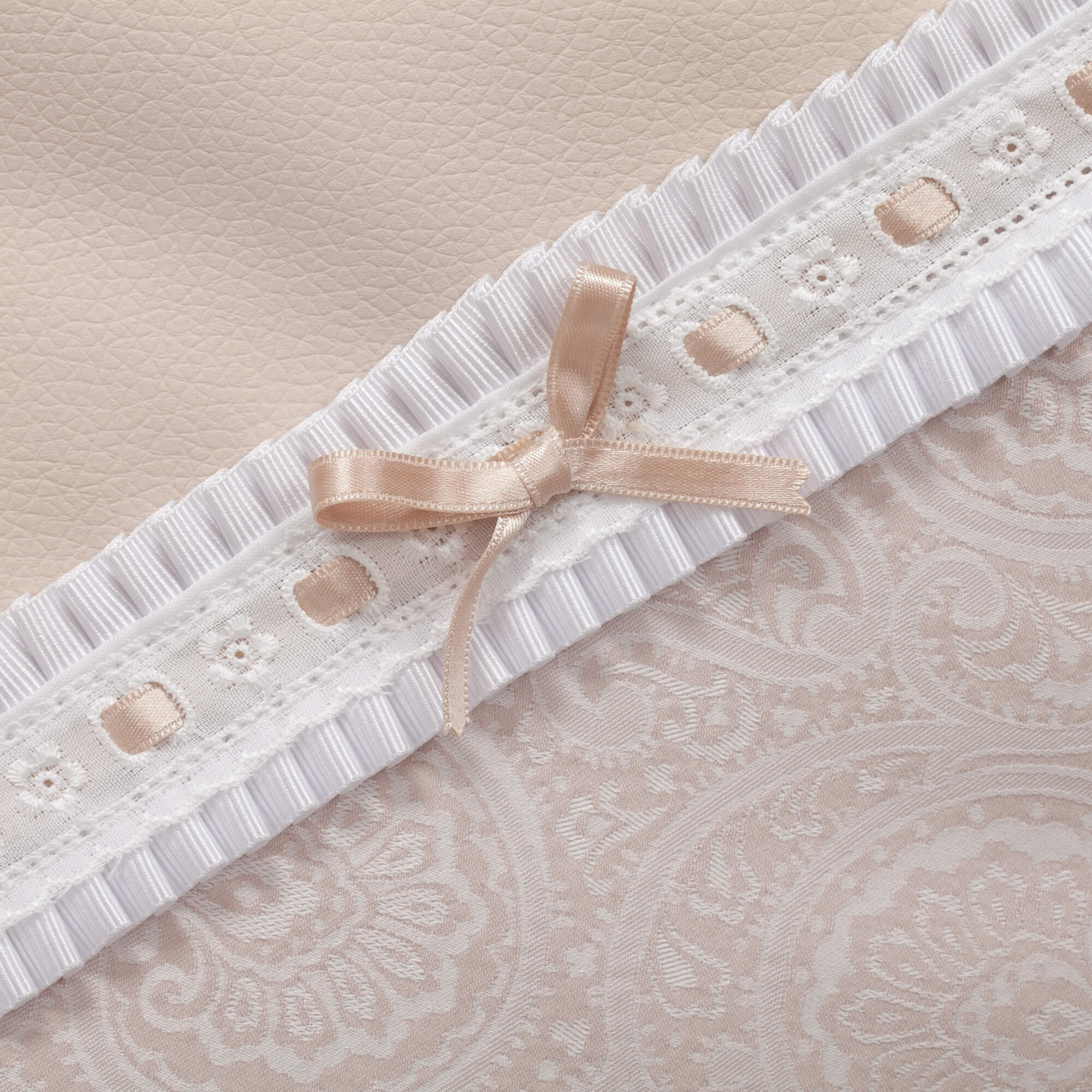 Primer plano de una tela beige con un borde de encaje blanco y un lazo de cinta beige en la esquina.