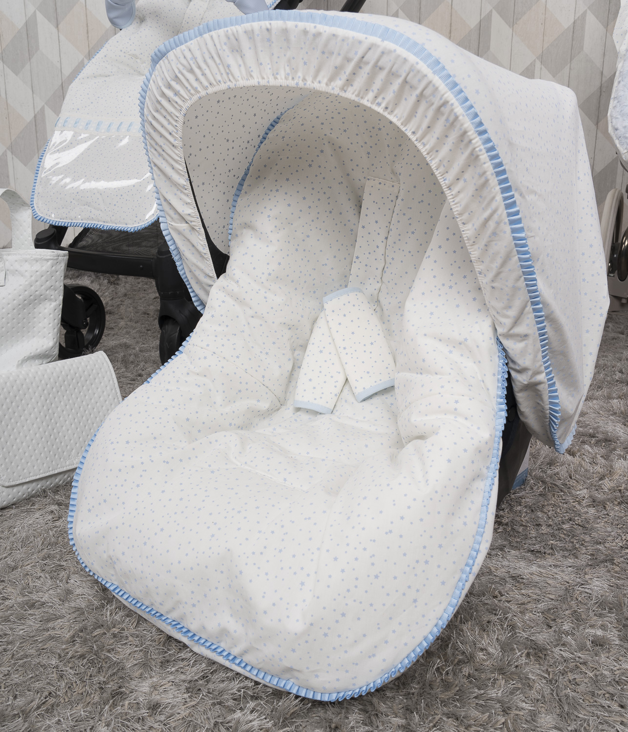 Asiento de cochecito de bebé cubierto de tela blanca con estrellas azules y ribete.