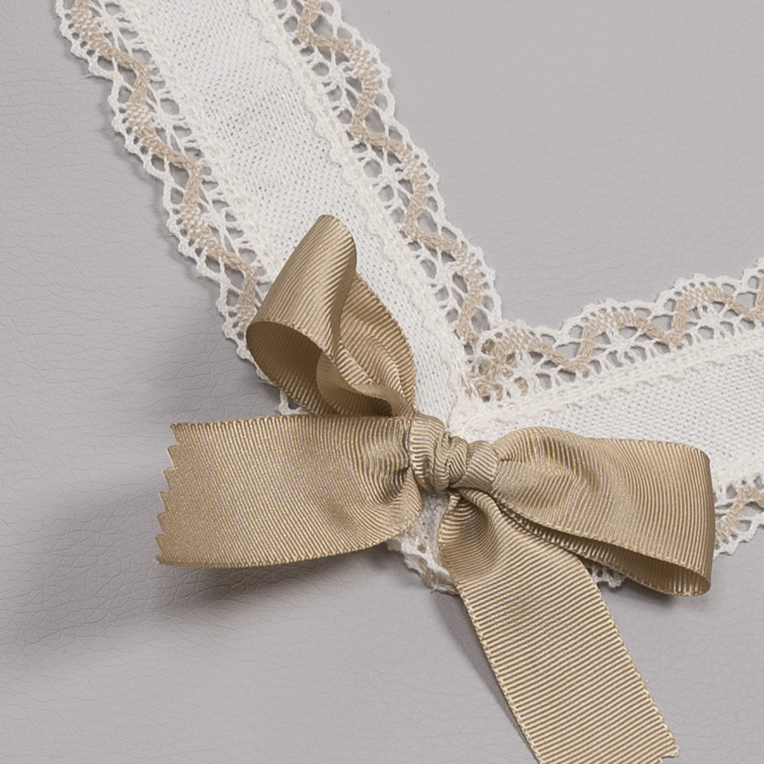 Cuello de punto blanco con ribete de encaje beige y lazo beige. Fondo gris.