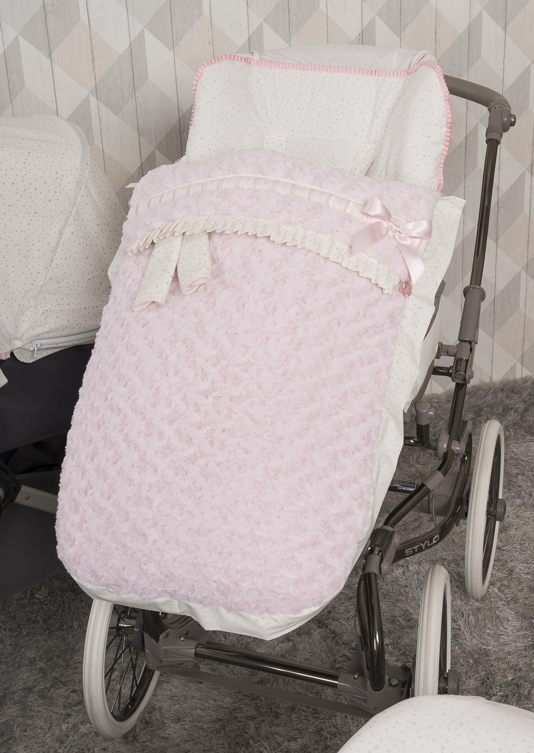 Un cochecito de bebé rosa con un saco de dormir floral rosa y detalles de encaje.