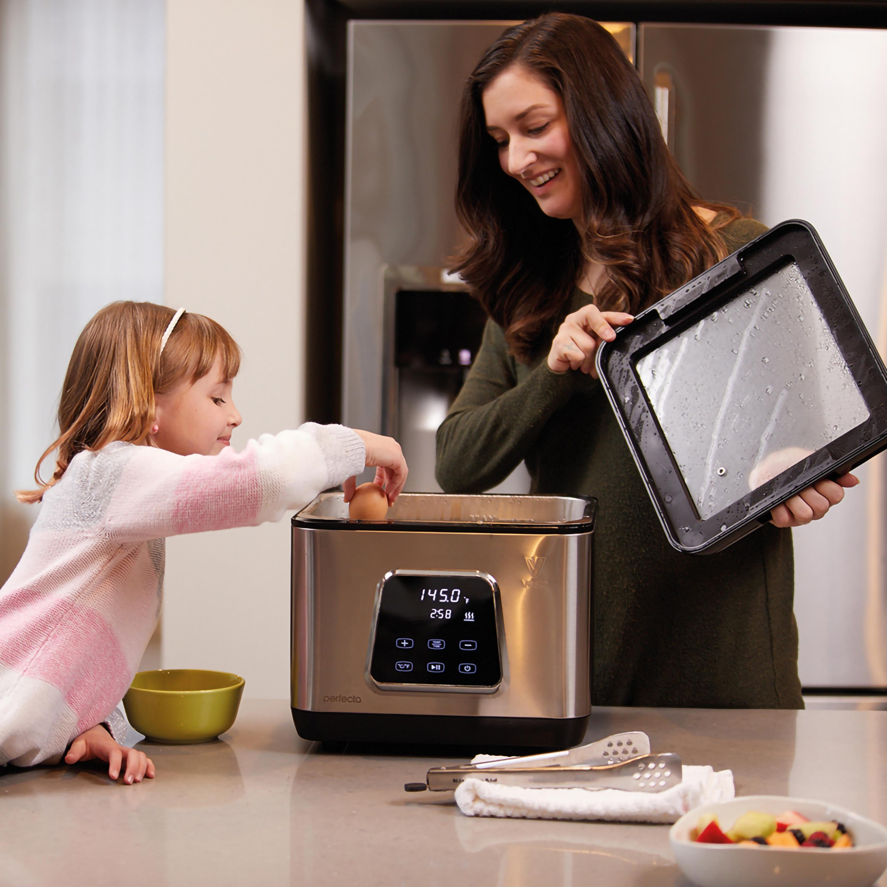 Una donna e una bambina usano una macchina sous vide, con ingredienti su un bancone.