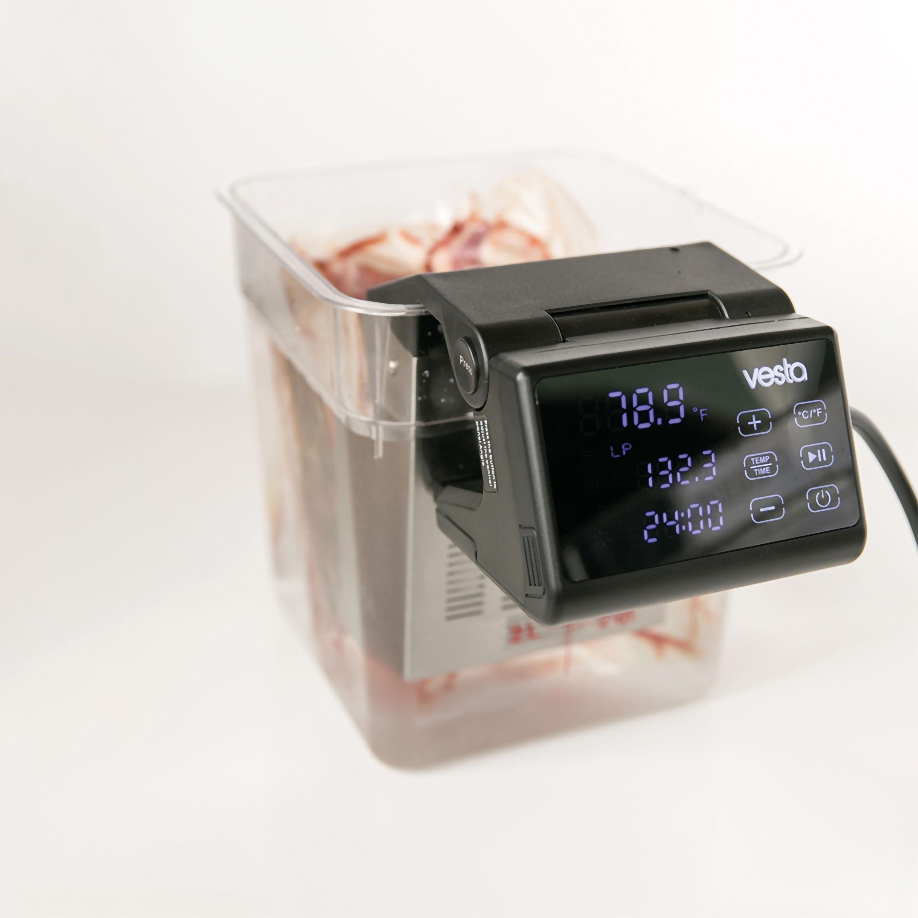 Una macchina per sous vide con pannello di controllo nero. È in un contenitore trasparente con cibo.