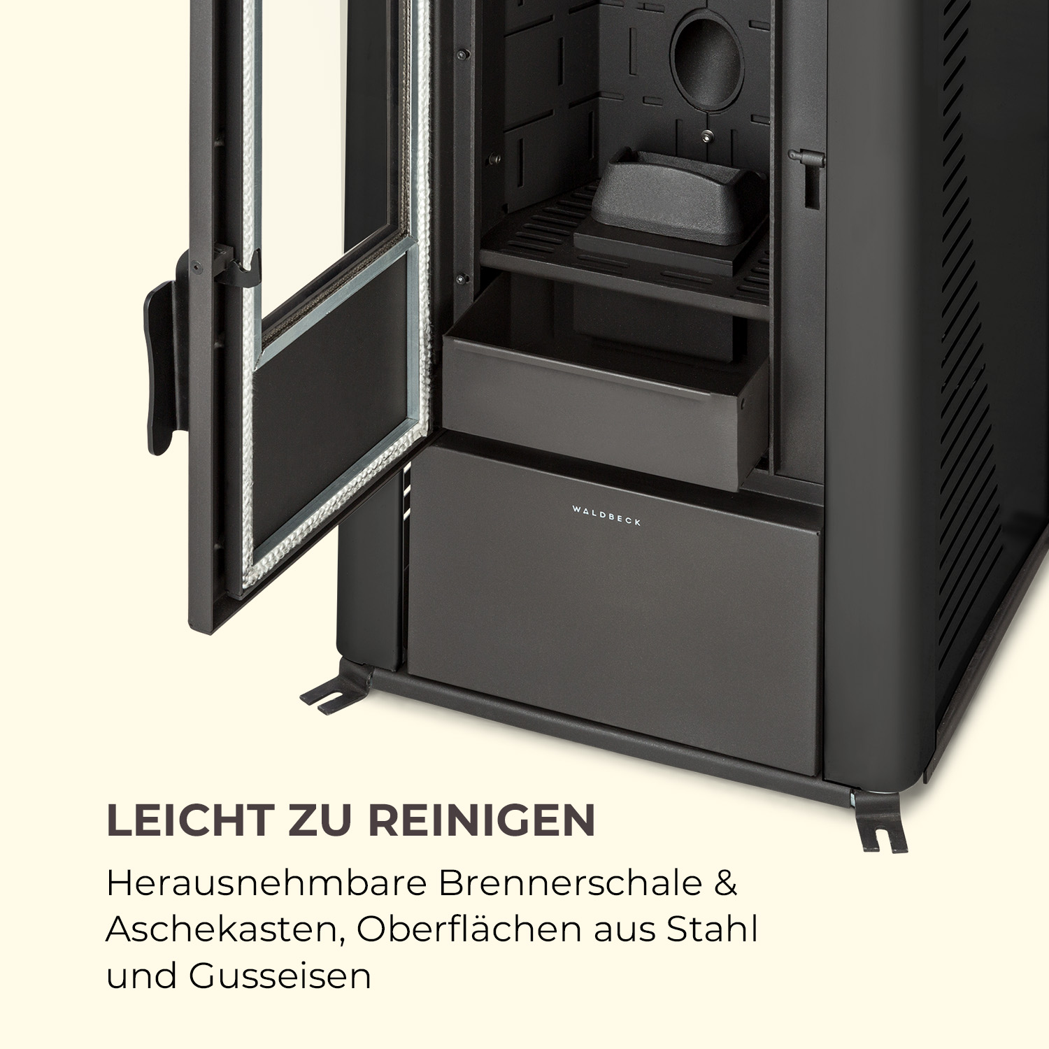 Schwarzer Metallofen mit offener Glastür. Merkmale sind eine herausnehmbare Brennerschale, Aschebox und Stahloberflächen. Marke: WALDBECK.