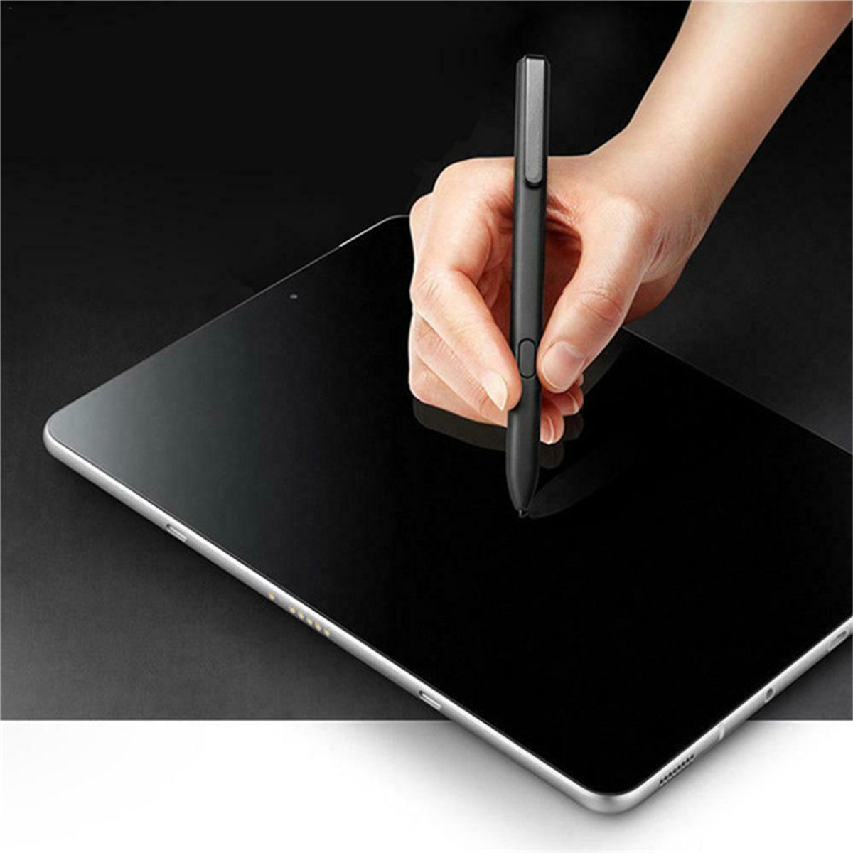 Eine Hand, die einen schwarzen Stift über einem schwarzen Tablet hält. Das Tablet hat einen weißen Rand.