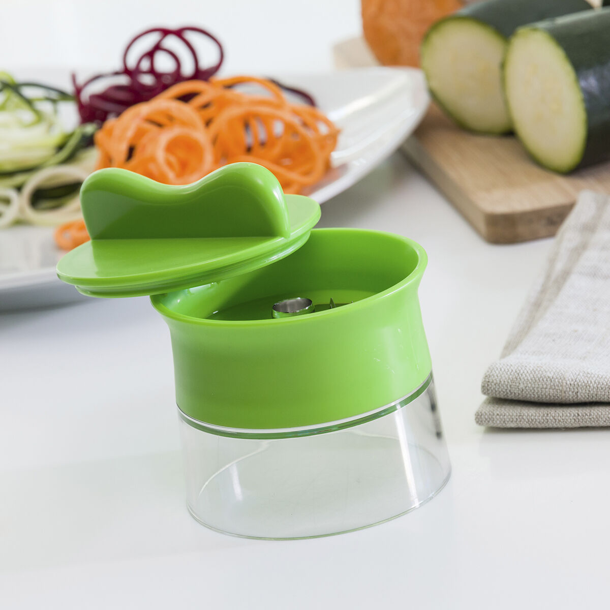 Uno spiralizzatore verde con verdure come zucchine e carote, e verdure a spirale su un piatto.