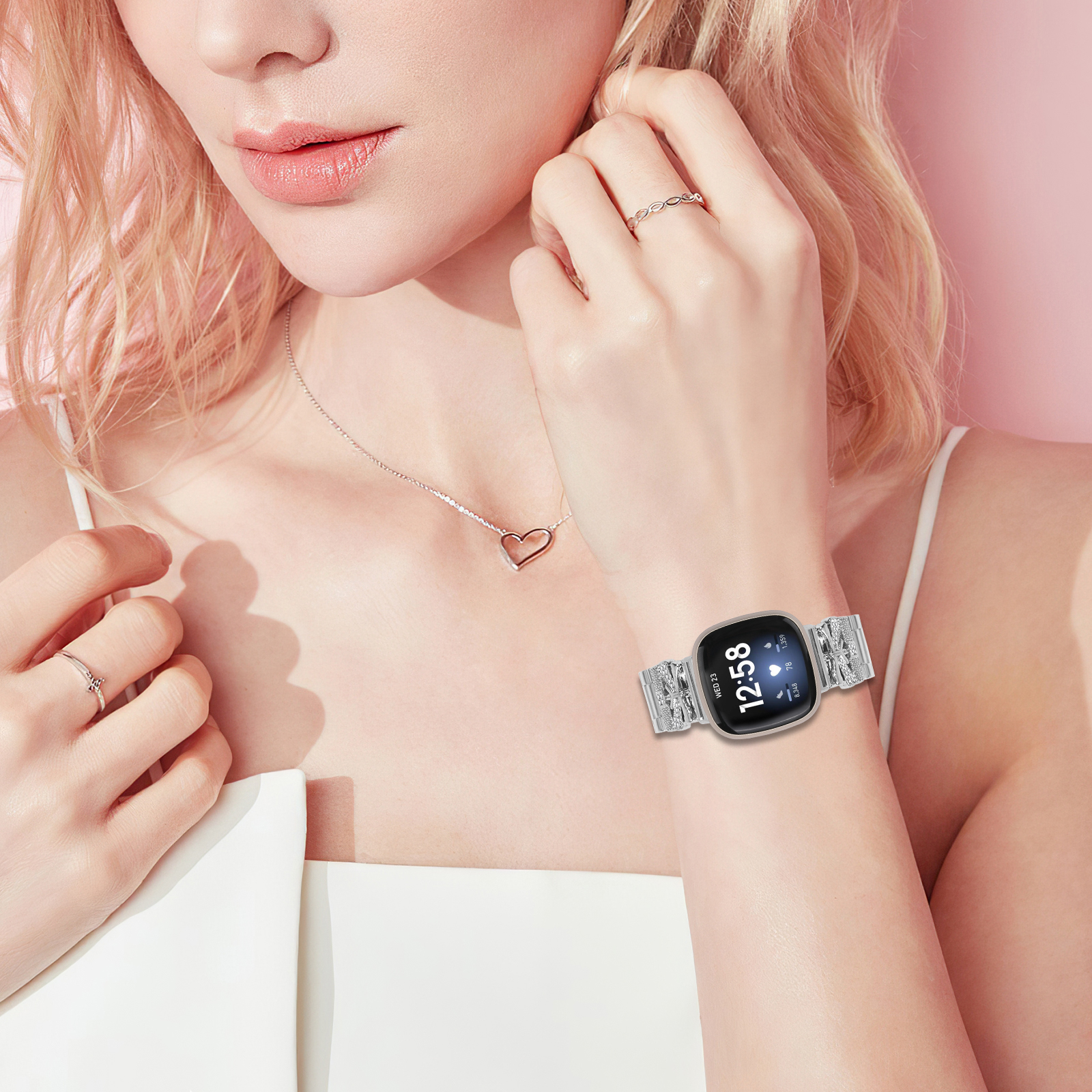 Eine Frau trägt eine Smartwatch am Handgelenk mit silbernem Band und Herz-Halskette.