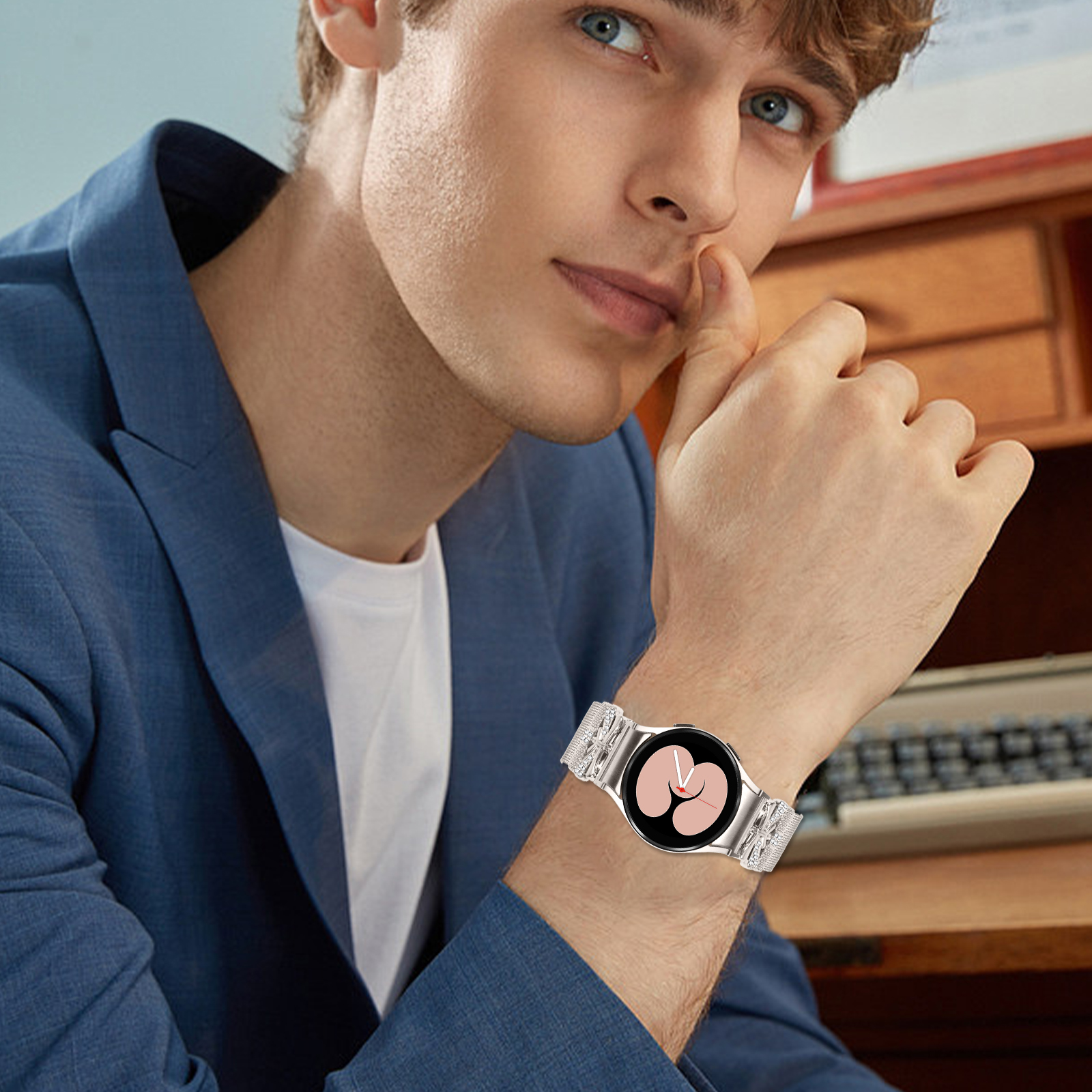 Mann, der einen blauen Blazer trägt, zeigt eine silberne Uhr mit weißem Armband. Er ist drinnen.