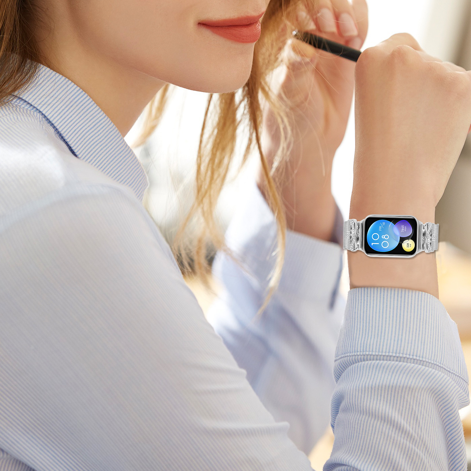 Donna con smartwatch con cinturino argentato, che tiene in mano una penna.