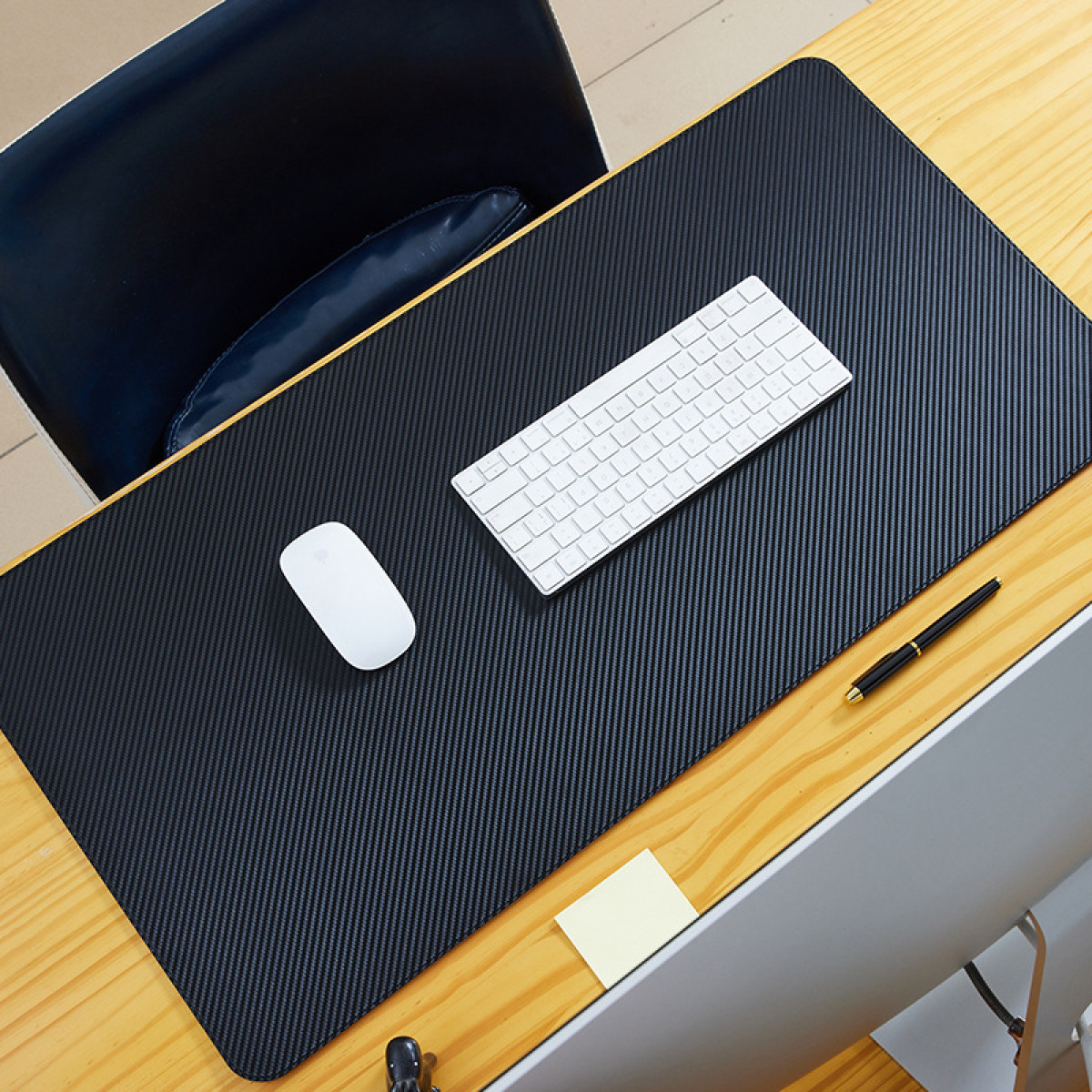 Schwarze Schreibtischunterlage mit weißer Tastatur, Maus, Stift und Haftnotiz, Draufsicht.
