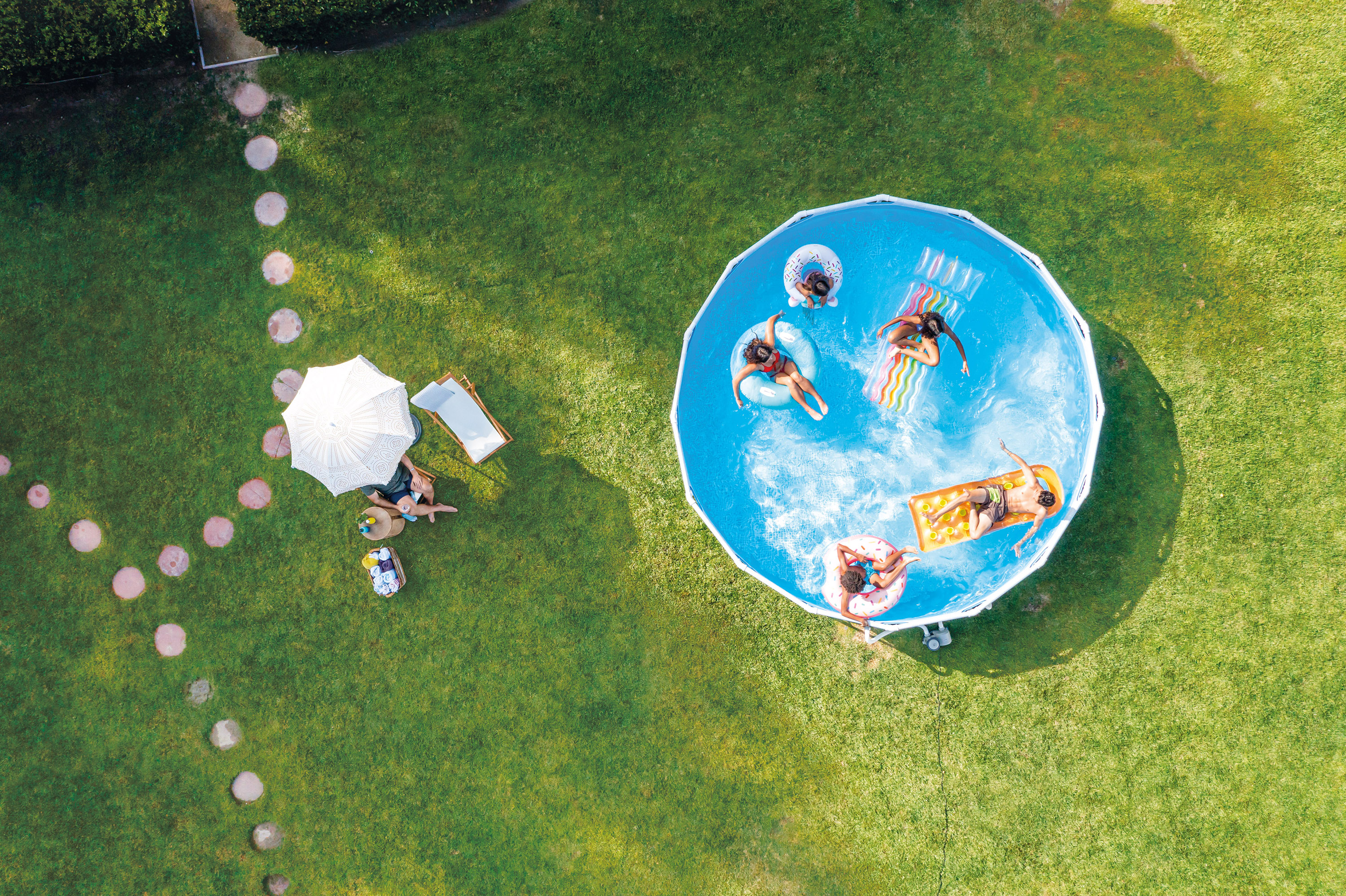 Vogelperspektive von Menschen in einem runden Pool, mit Sonnenanbetern auf dem Rasen.