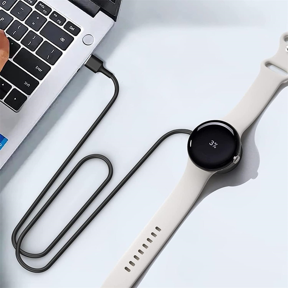 Eine schwarze Uhr, die über ein USB-Kabel von einem Laptop aufgeladen wird. Die Uhr zeigt 3 % geladen.