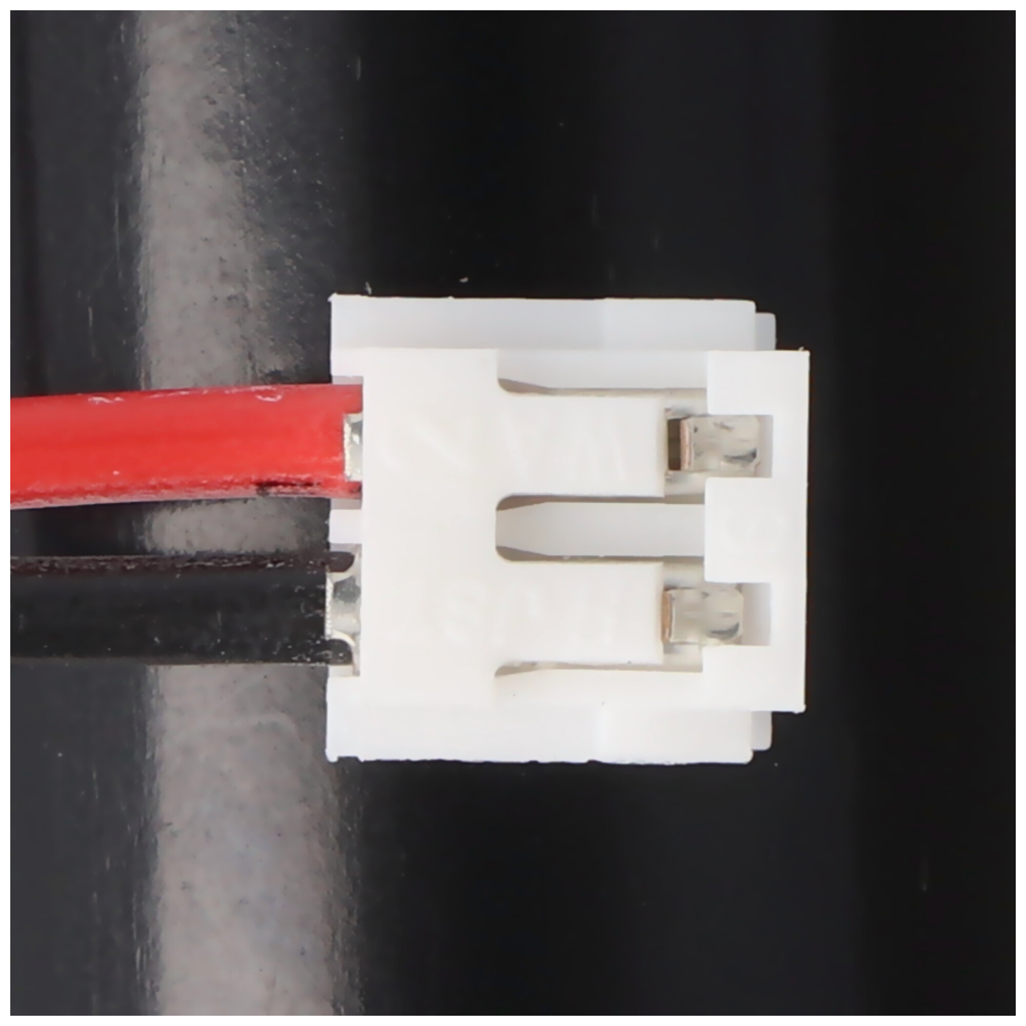 Nahaufnahme eines weißen elektrischen Steckers mit roten und schwarzen Drähten, auf schwarzem Hintergrund.
