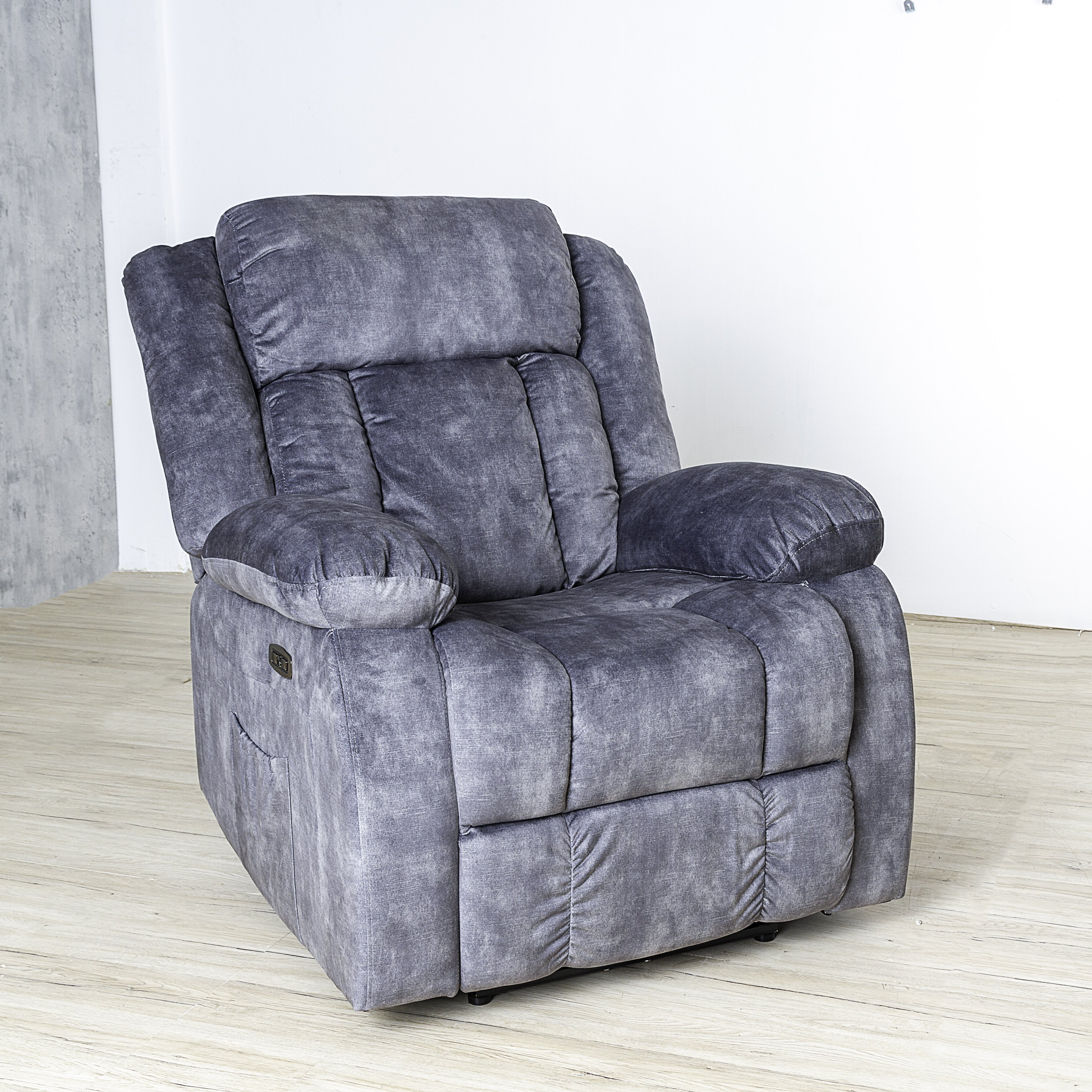 Una silla reclinable gris sobre un suelo de madera clara. La pared es blanca.