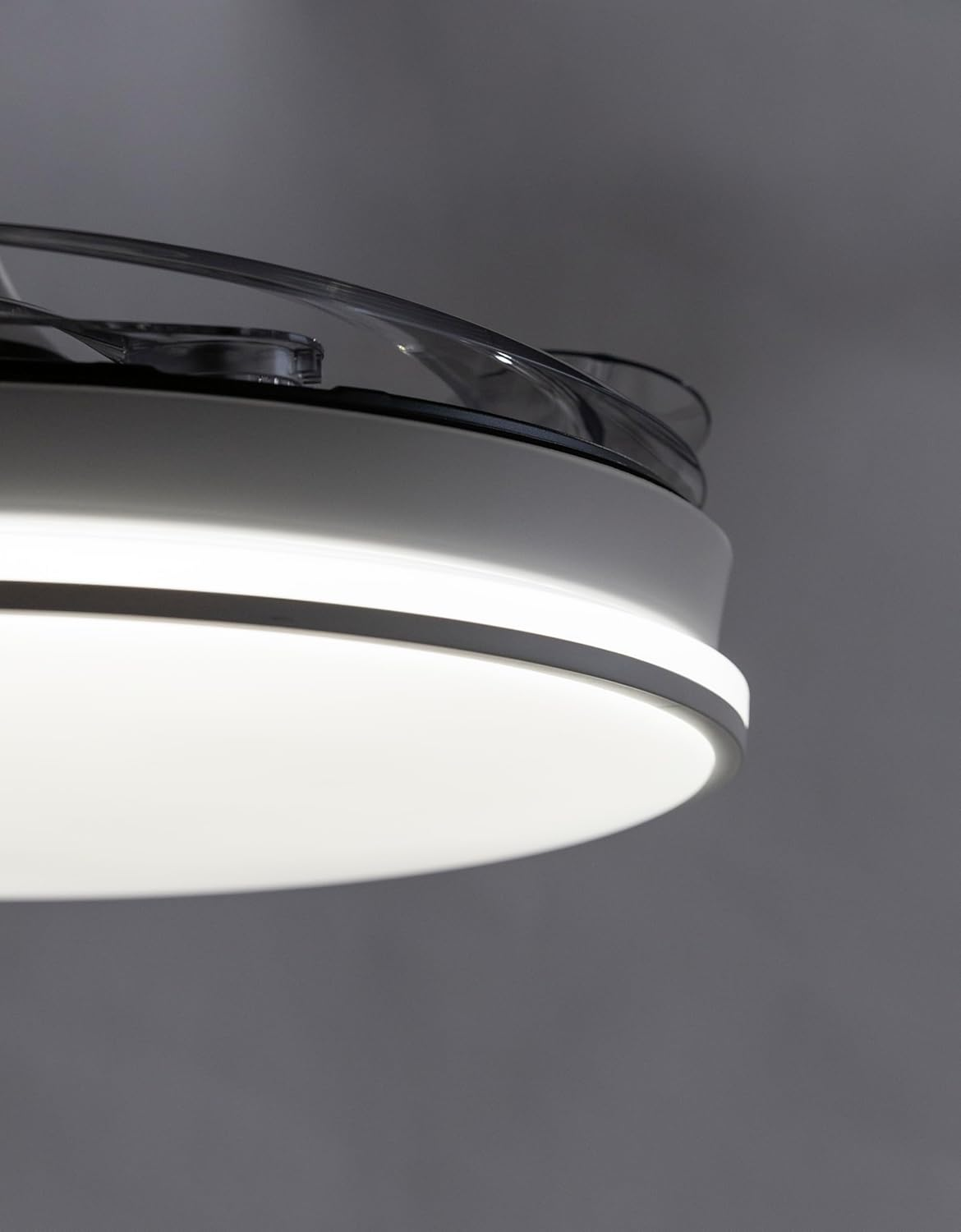 Primer plano de una luz de ventilador de techo blanca circular sobre fondo gris.
