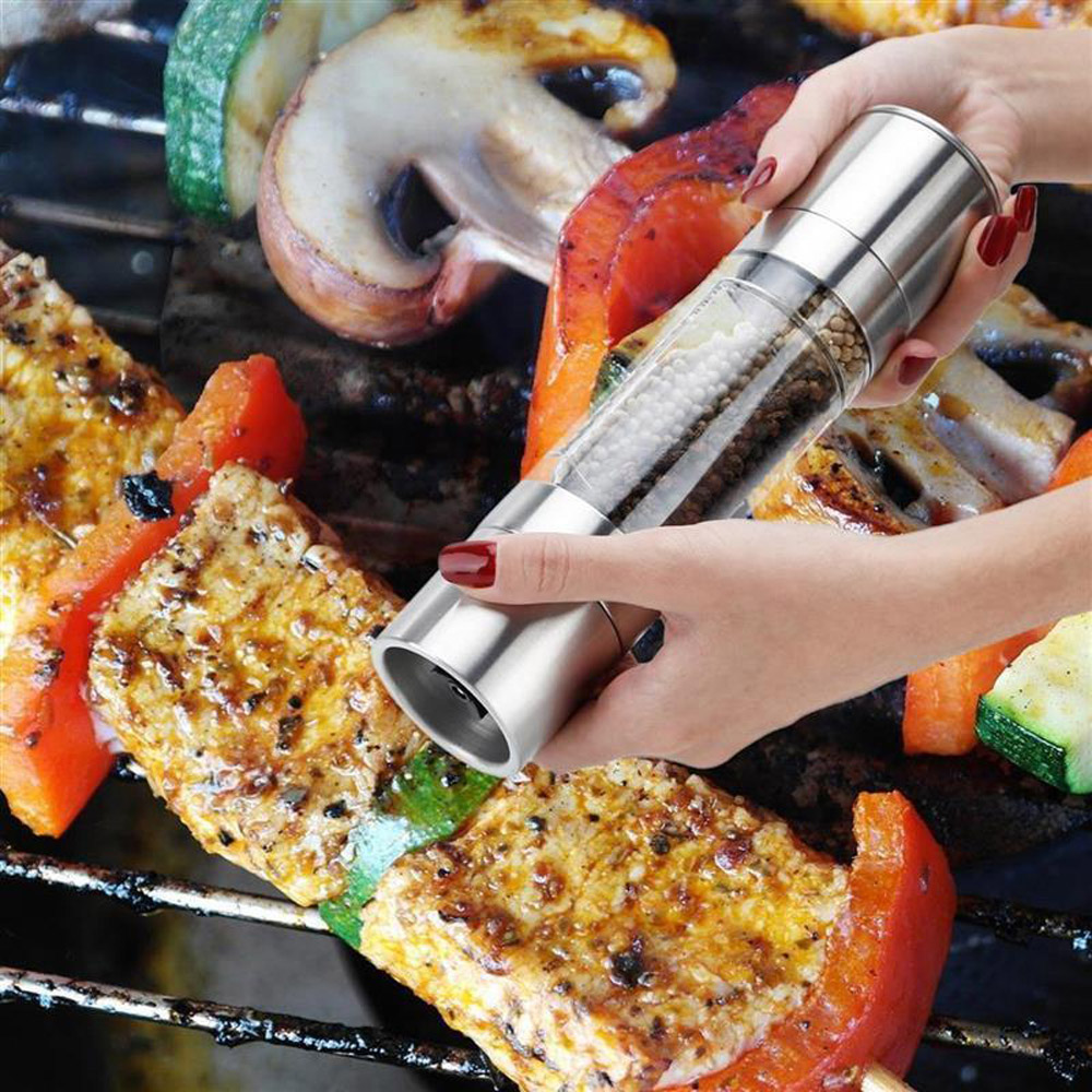 Eine Person mahlt Pfeffer auf gegrilltes Gemüse.