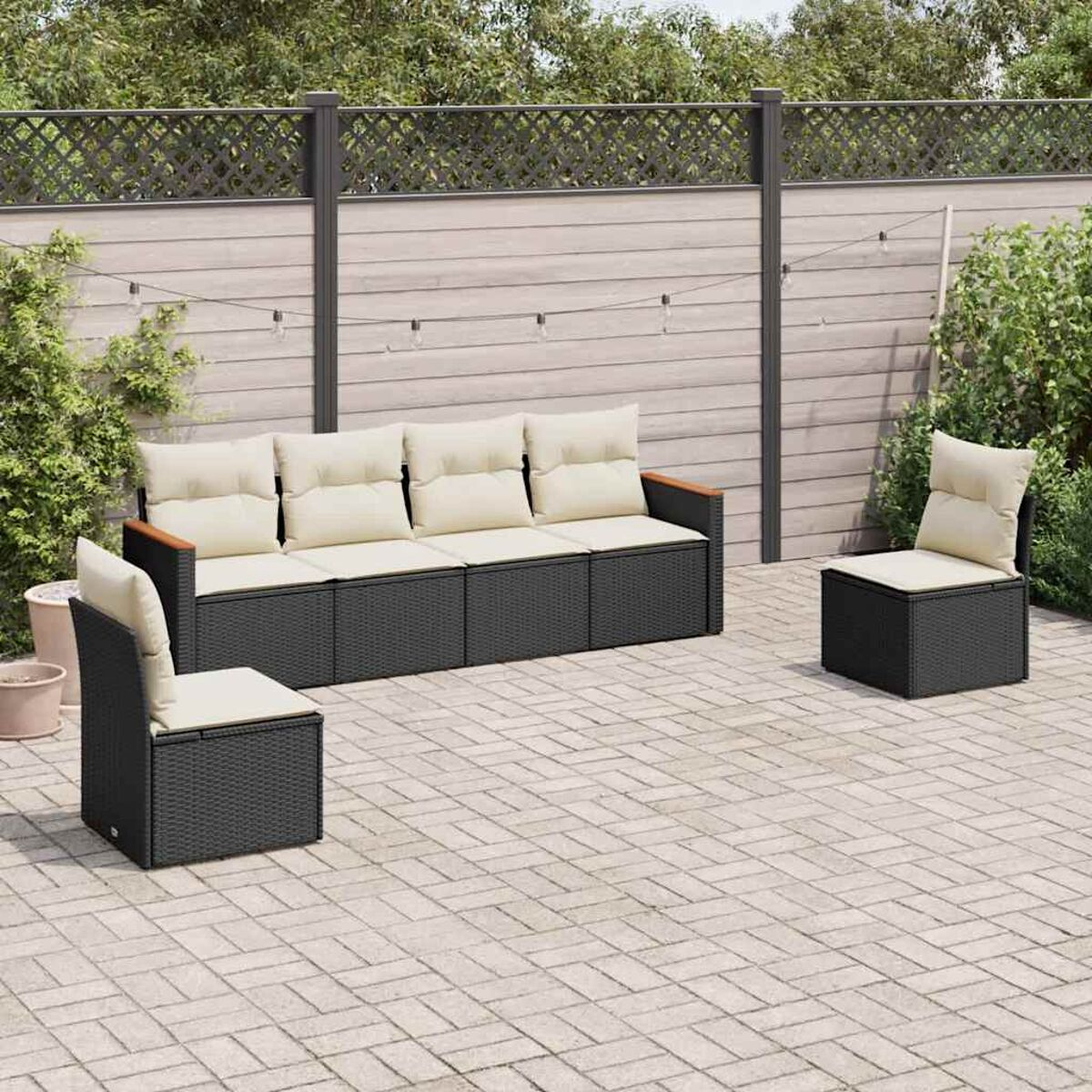 Terrassenmöbel-Set: ein langes Sofa und zwei Stühle, alles schwarzes Korbgeflecht mit beigen Kissen. Gepflasterte Terrasse.