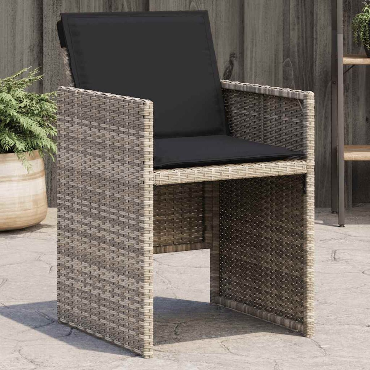 Stuhl im Rattan-Stil für draußen mit schwarzem Kissen, auf einer Terrasse platziert.