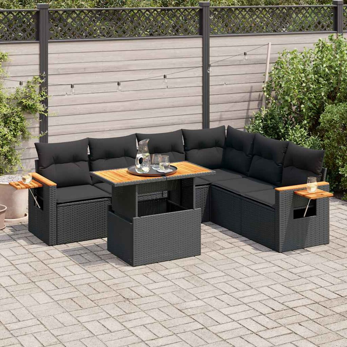 Schwarzes Outdoor-Sofa mit Kissen, Holztisch, Getränken und einem umzäunten Hintergrund.