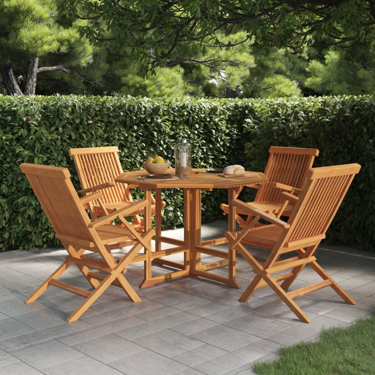 Vier hölzerne Klappstühle umrunden einen quadratischen Holztisch auf einer Stein-Terrasse, mit einem grünen Heckenhintergrund.