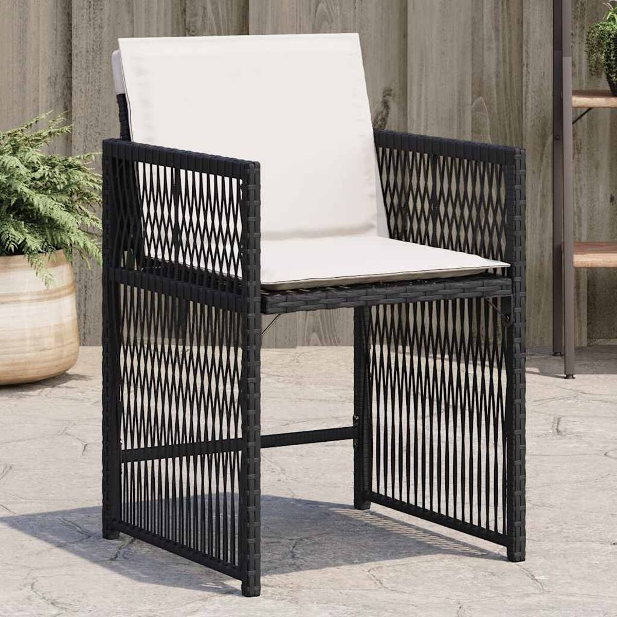 Sedia in vimini nera con cuscino bianco, all'aperto su pietre del patio.