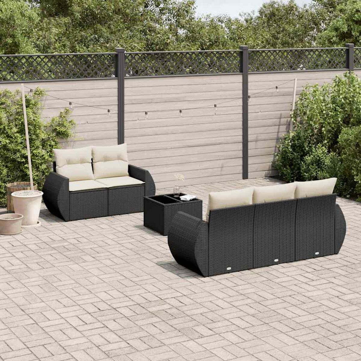 Eine schwarze Sitzgruppe im Freien auf einer Ziegelterrasse. Enthält ein Sofa, eine Doppelsitzer und einen Tisch.