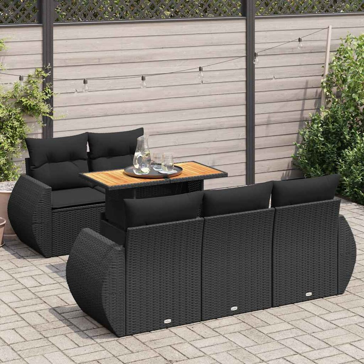 Set divani neri per esterni con un tavolo. Il set è su un patio. Lo sfondo presenta una recinzione e delle piante.