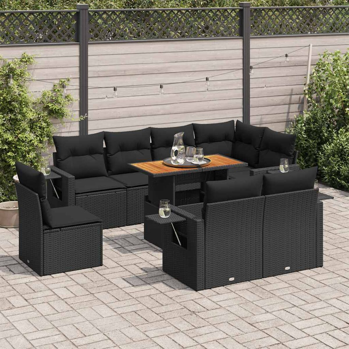 Schwarzes Rattan-Sofa-Set mit Kissen, Tisch und Stühlen auf einer Terrasse.