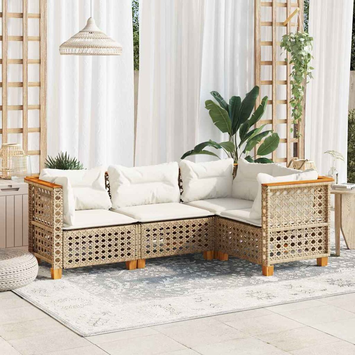 Divano in rattan beige con cuscini bianchi, su un tappeto, con tende bianche sullo sfondo.