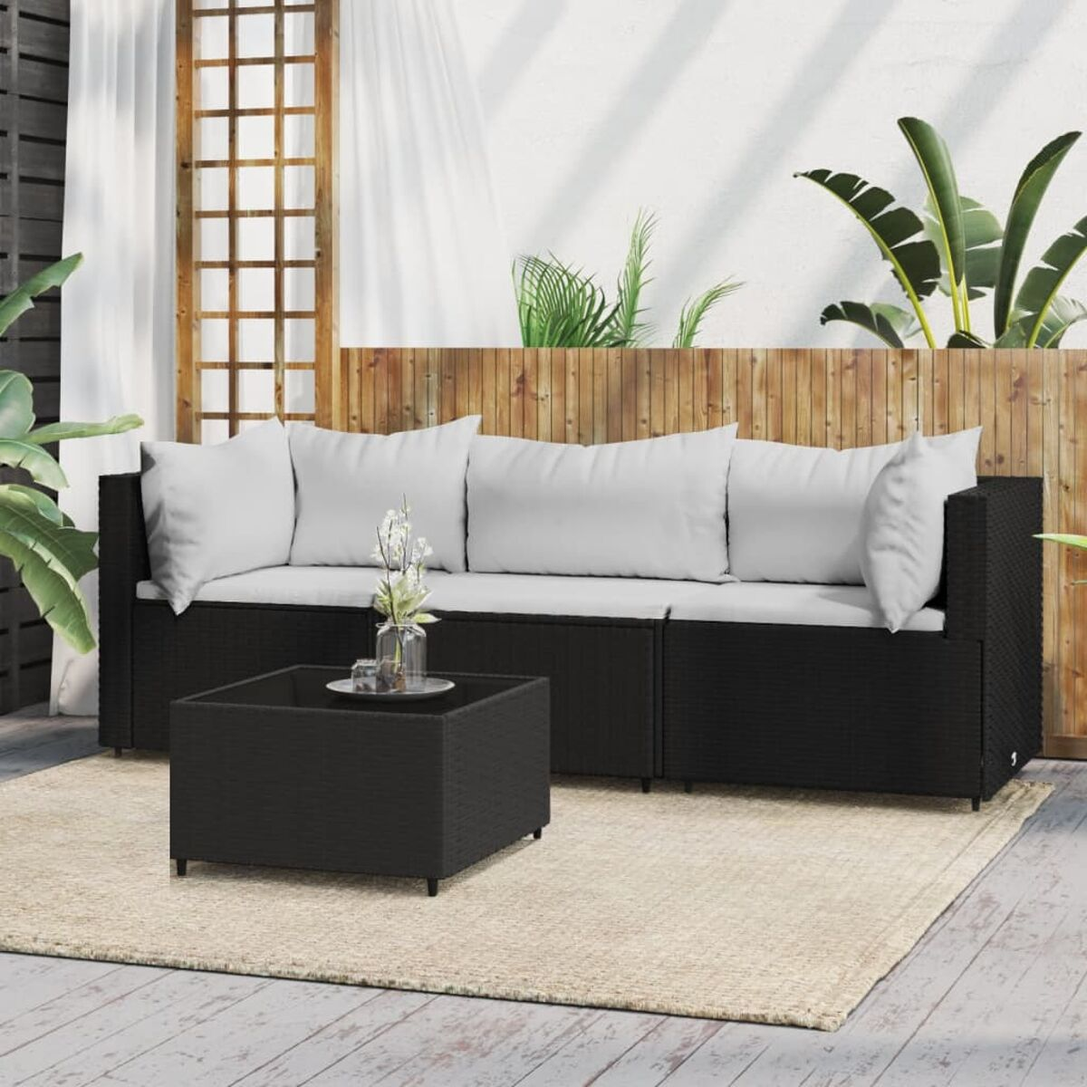 Schwarzes Outdoor-Sofaset mit weißen Kissen und einem schwarzen Tisch. Beiger Teppich, Holzzaun.