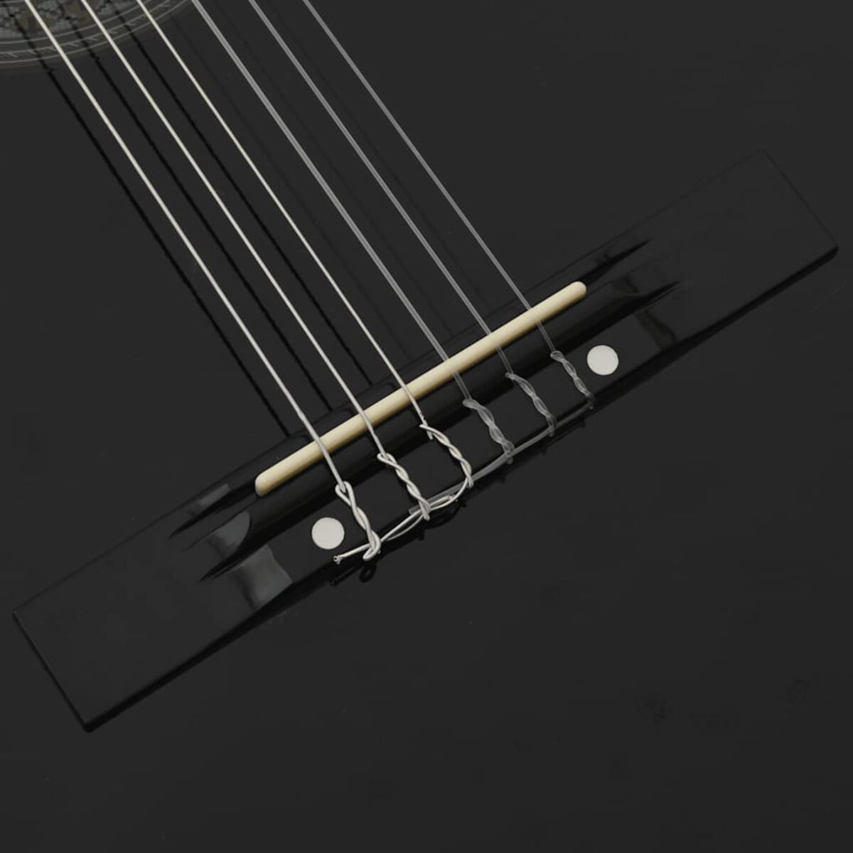 Nahaufnahme der Brücke einer schwarzen Gitarre mit Saiten. Die Saiten sind silber, die Brücke schwarz.