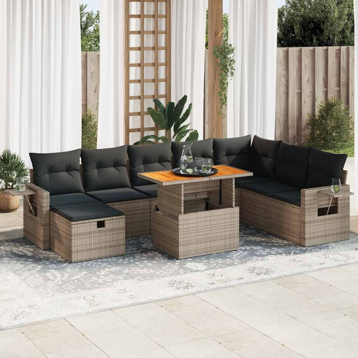 Un set da patio con un tavolo, un divano componibile con cuscini grigi e un tappeto. Piante sullo sfondo.