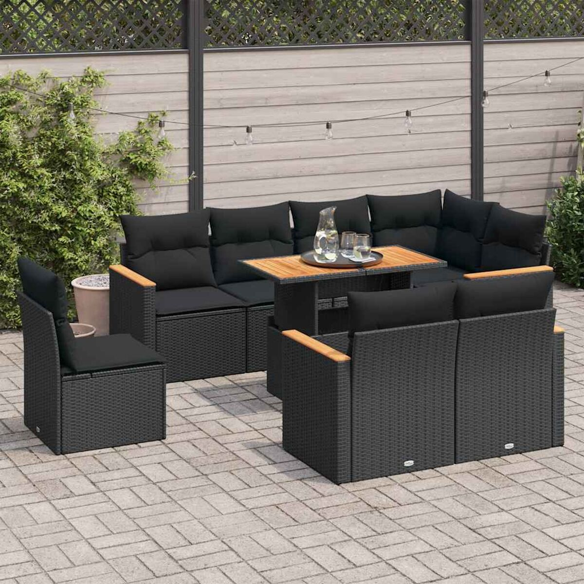 Set di mobili da esterno in vimini nero con cuscini e tavolo in legno, su un patio in pietra.