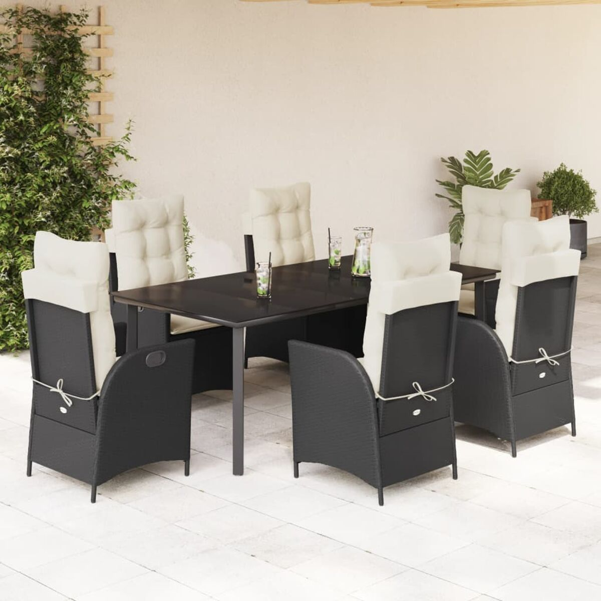 Essgruppe im Freien. Schwarze Stühle mit beigefarbenen Kissen um einen dunklen Tisch. Pflanzen im Hintergrund.